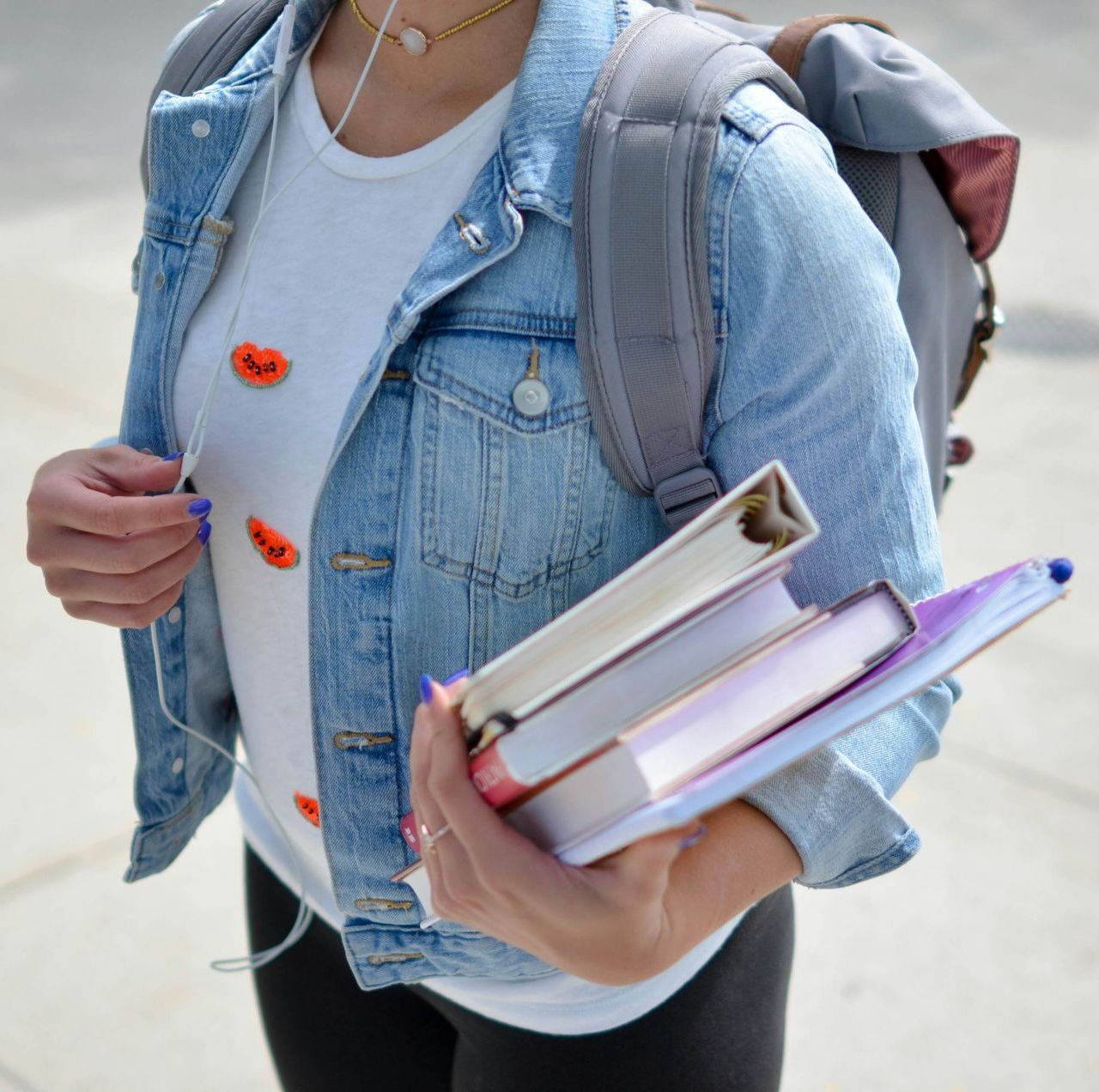 A woman in a denim jacket is holding a stack of books