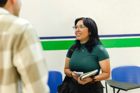 A woman is talking to a man in a classroom while holding a book.