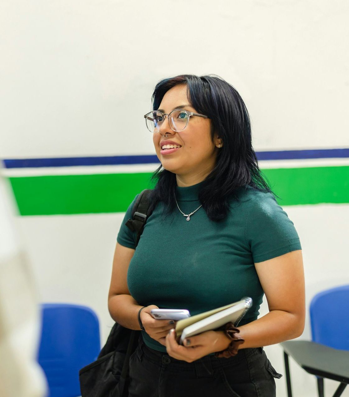 A woman wearing glasses and a green shirt is holding a book and a cell phone.