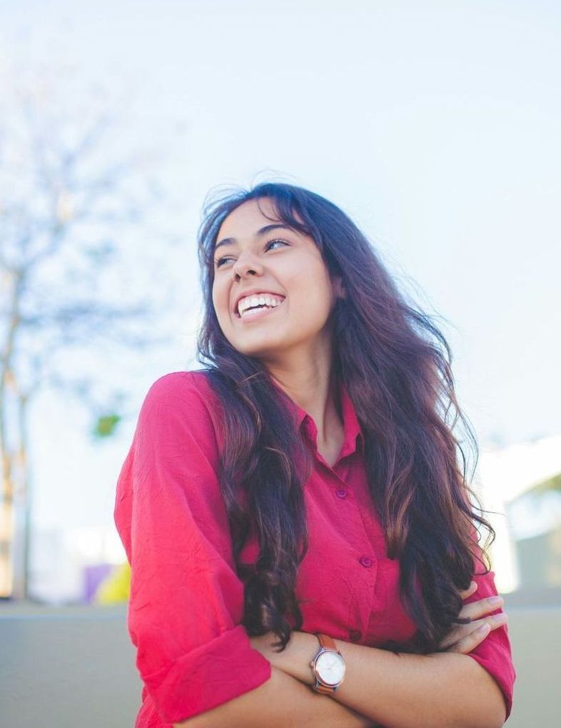 A woman in a red shirt is smiling with her arms crossed.