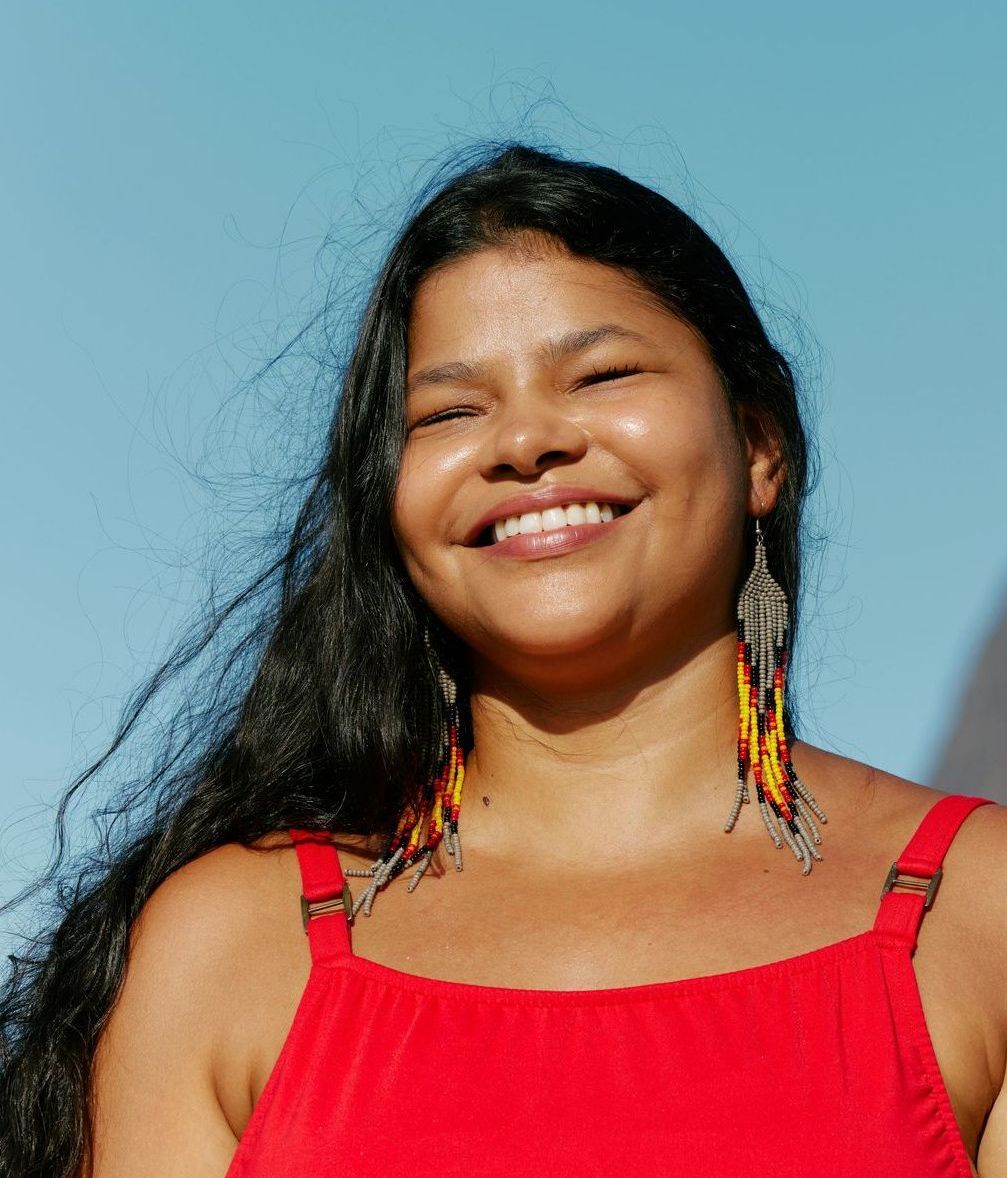 A woman wearing a red tank top and earrings is smiling