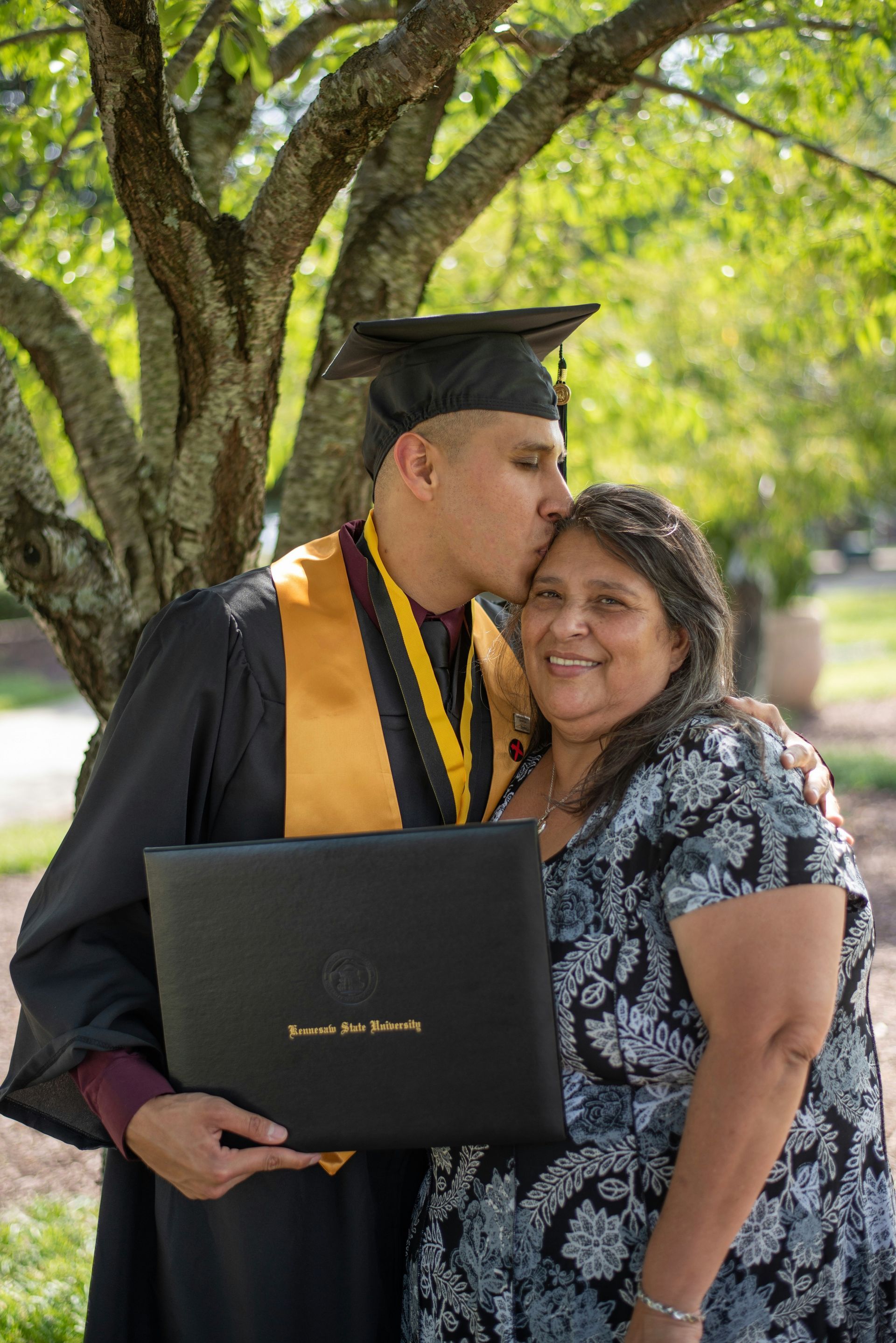 A man in a graduation cap and gown is kissing a woman on the cheek.