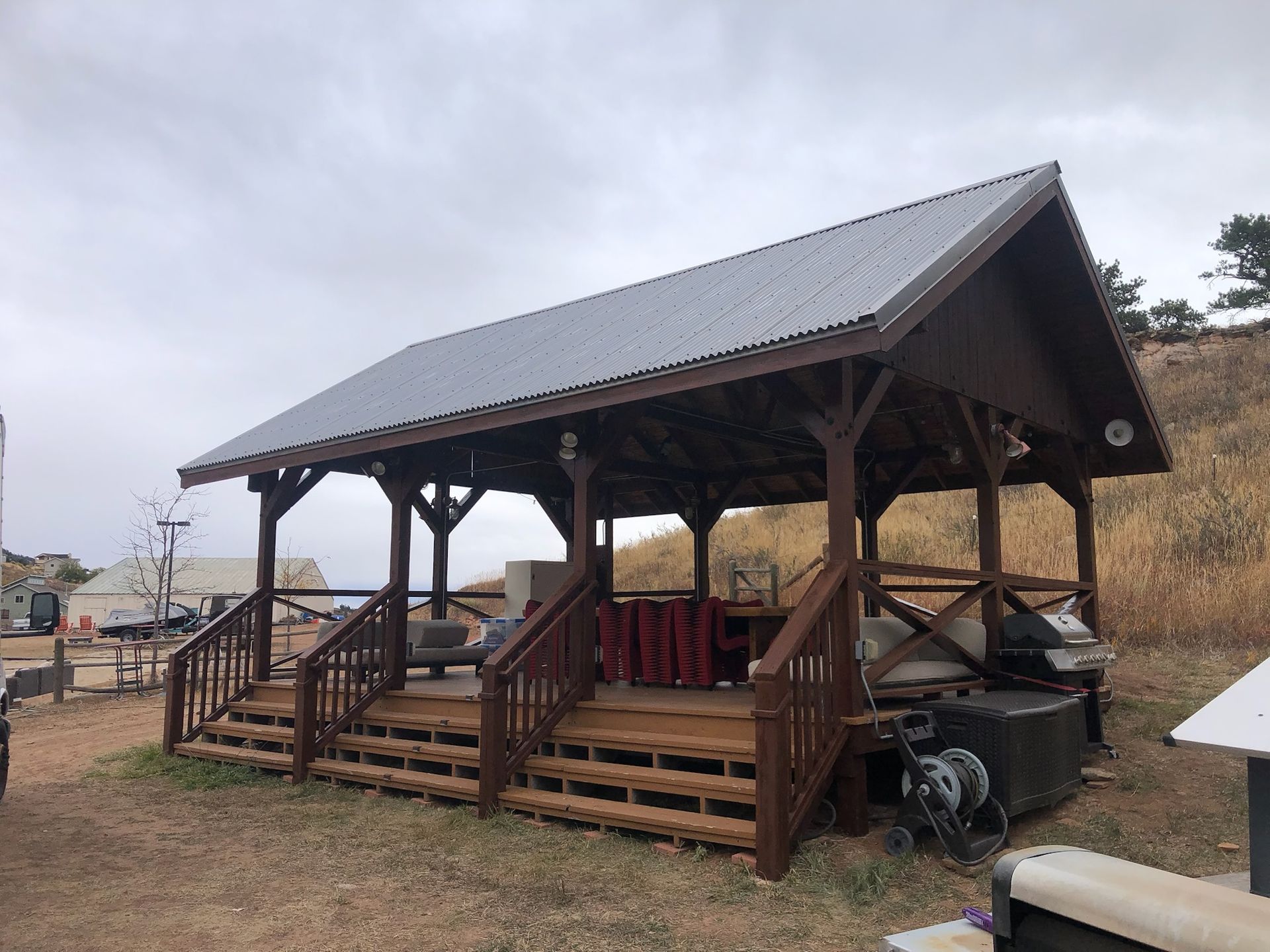 A wooden gazebo with a metal roof is sitting in the middle of a field.