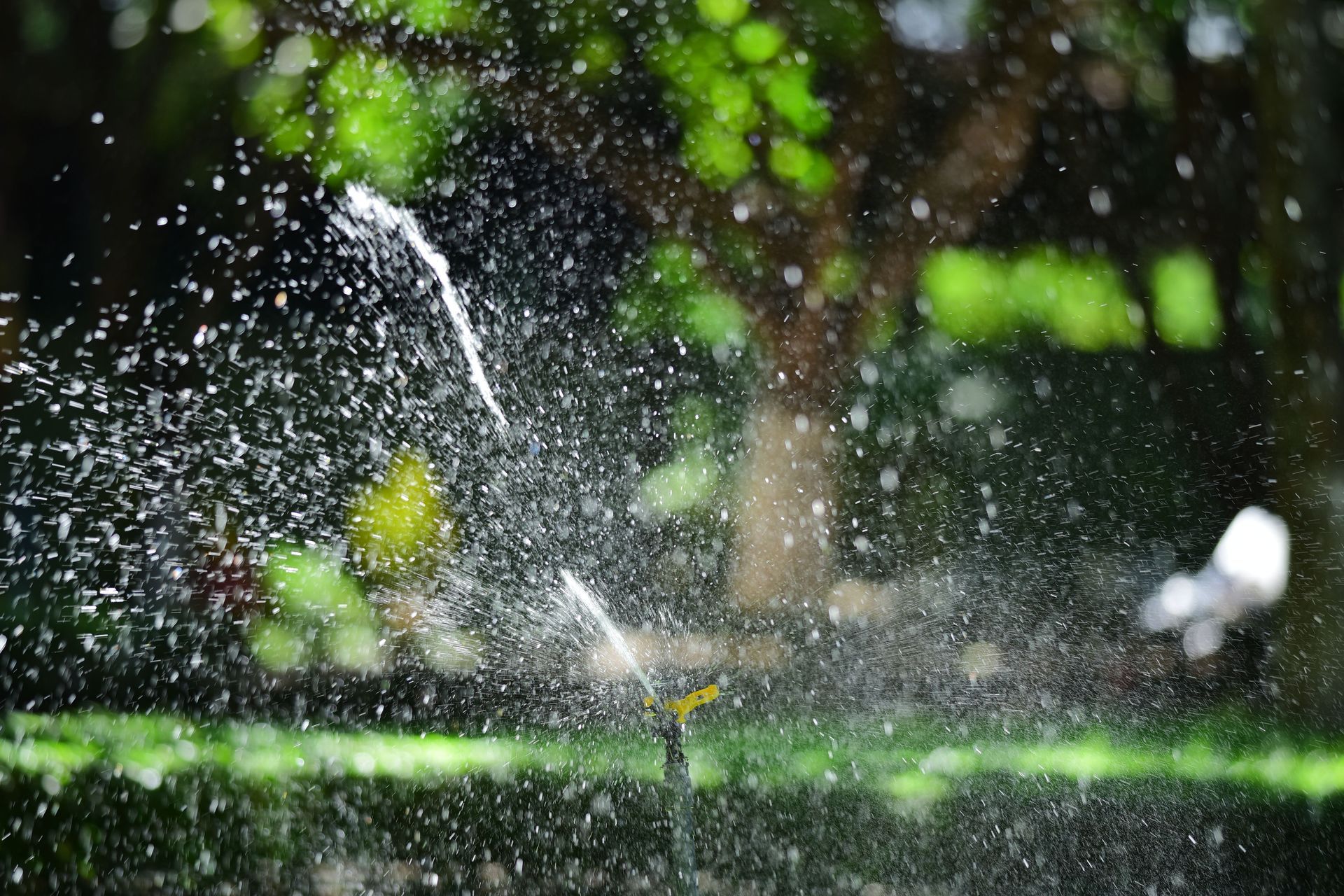 Lawn sprinkler spraying water in front of a tan building under a clear sky