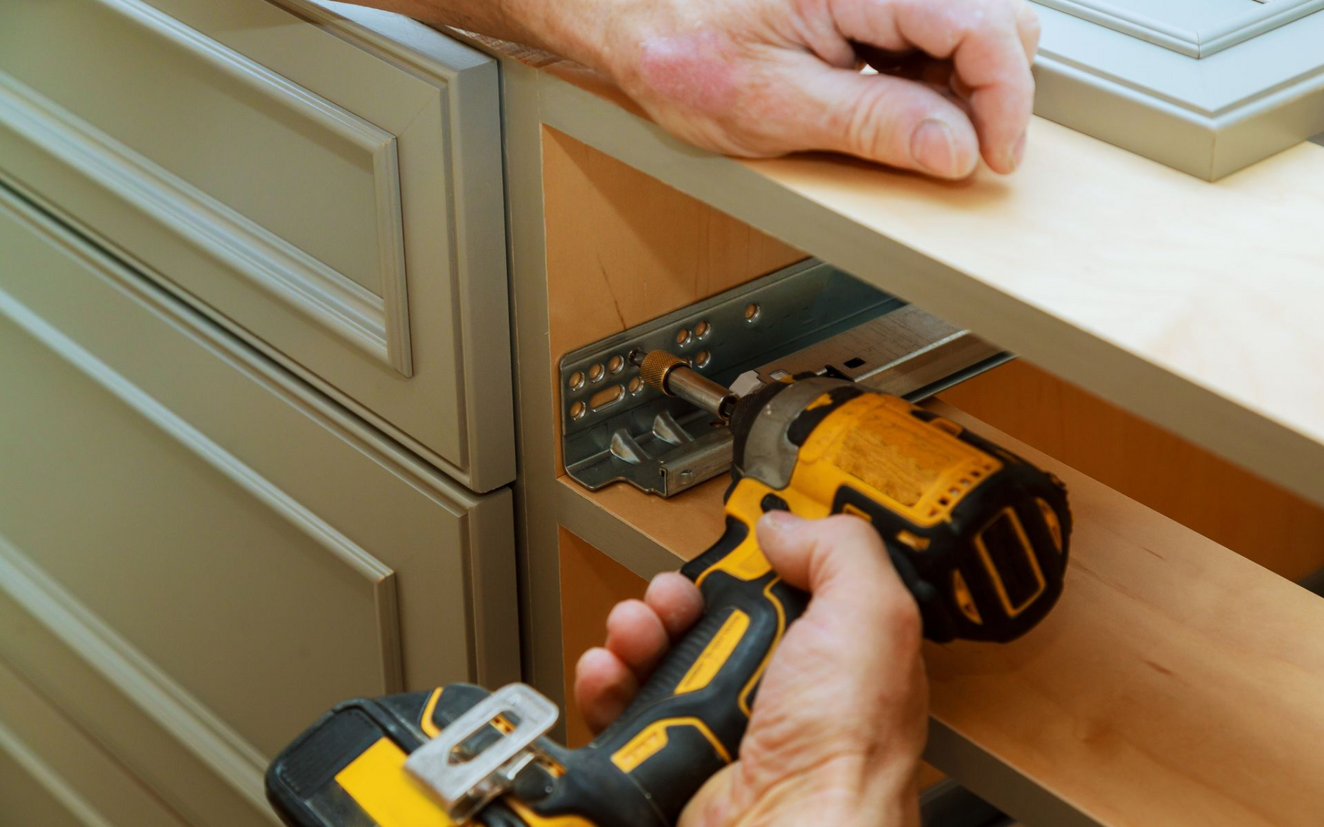 Person using a yellow drill to install a drawer slide inside a cabinet.