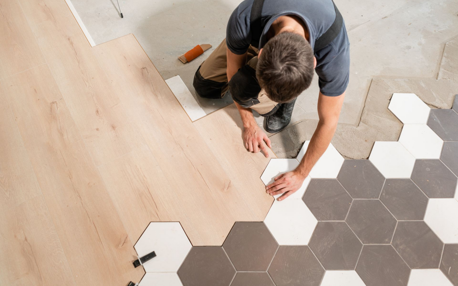 Person installing flooring, placing wood plank next to hexagonal tile pattern.