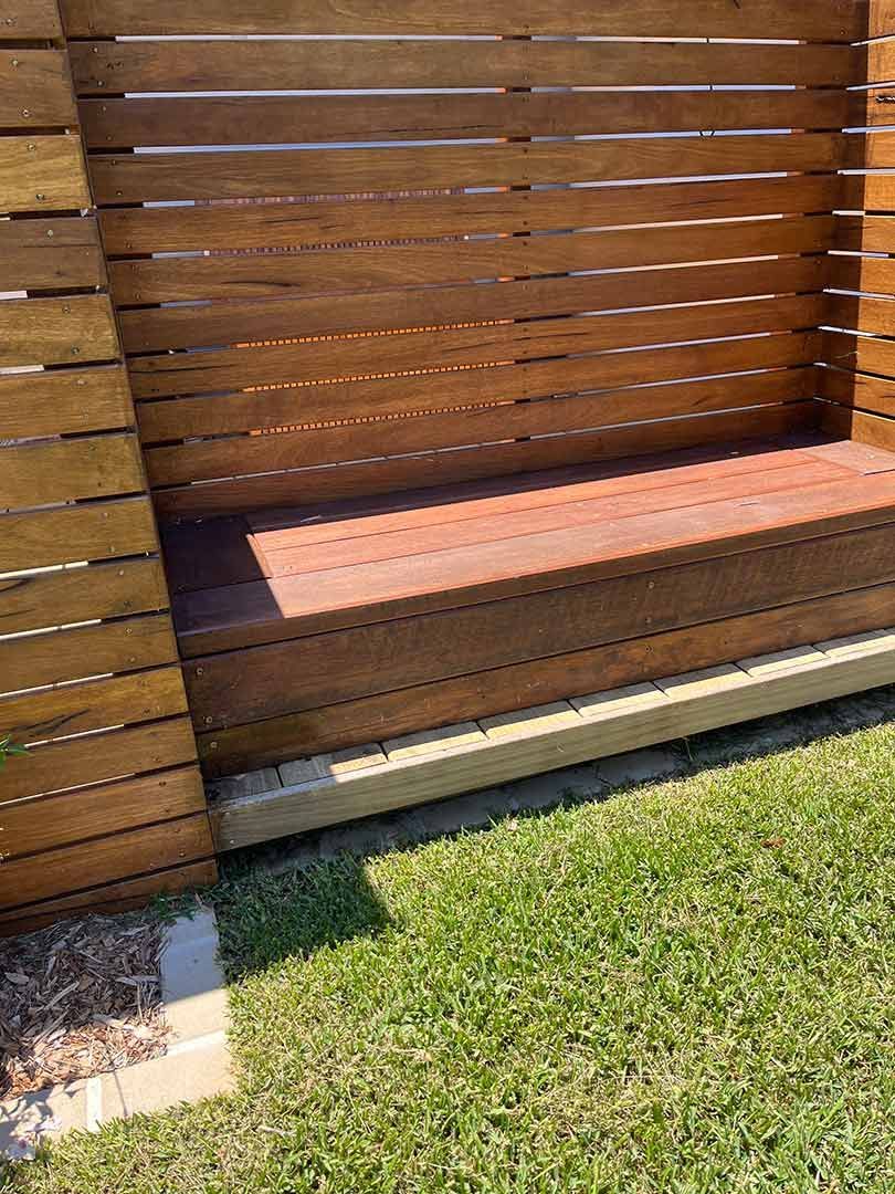 A Wooden Bench Is Sitting In The Grass Next To A Wooden Fence — Gnomes Landscape & Garden Supplies In Harrington, NSW