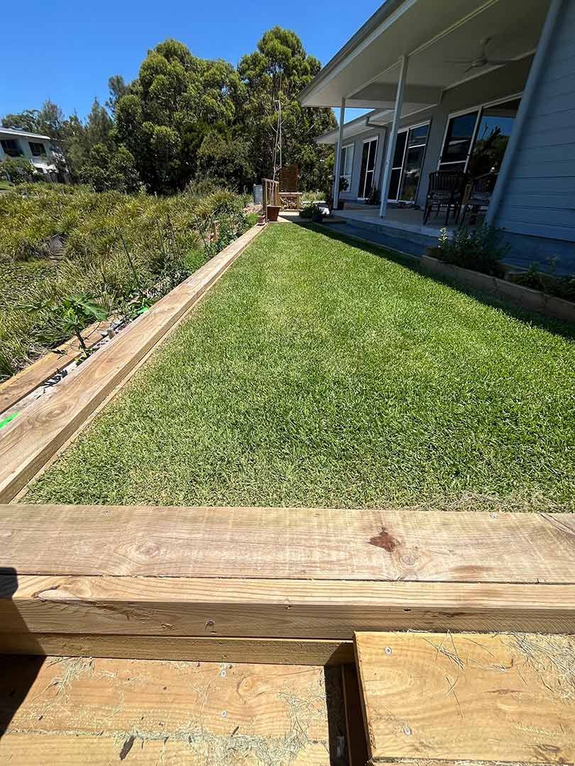 A Lush Green Lawn With A Wooden Fence In Front Of A House — Gnomes Landscape & Garden Supplies In Wingham, NSW