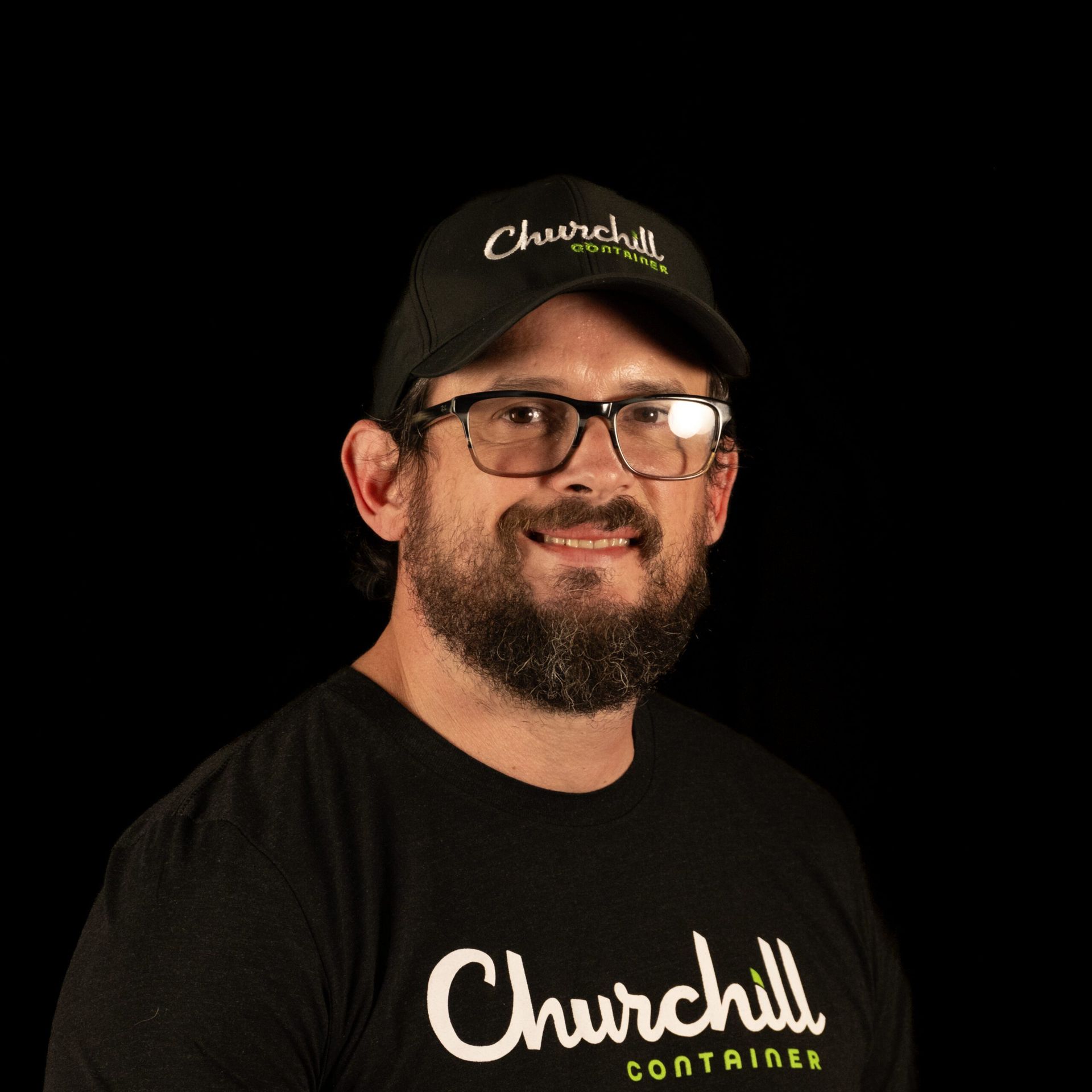 Man wearing glasses and a Churchill Containers hat and t-shirt, smiling, against a black background.