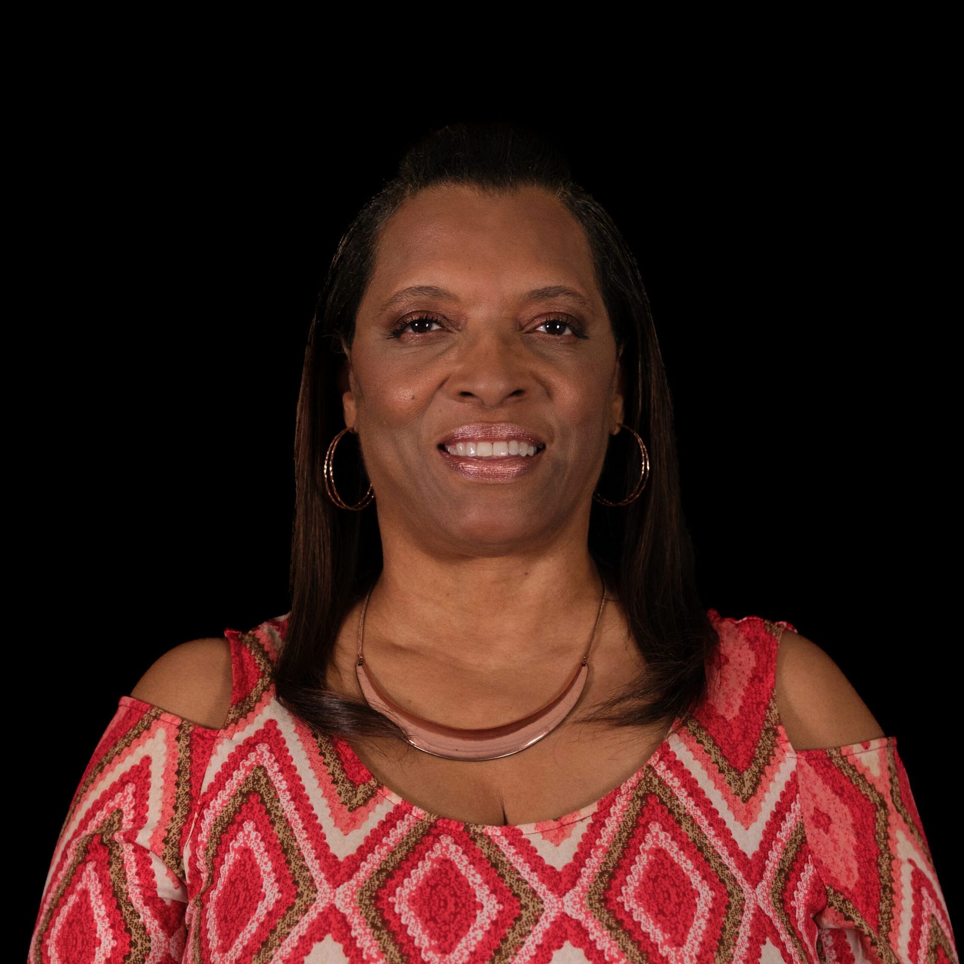 Woman with long brown hair, wearing a red and white patterned top, smiles. 