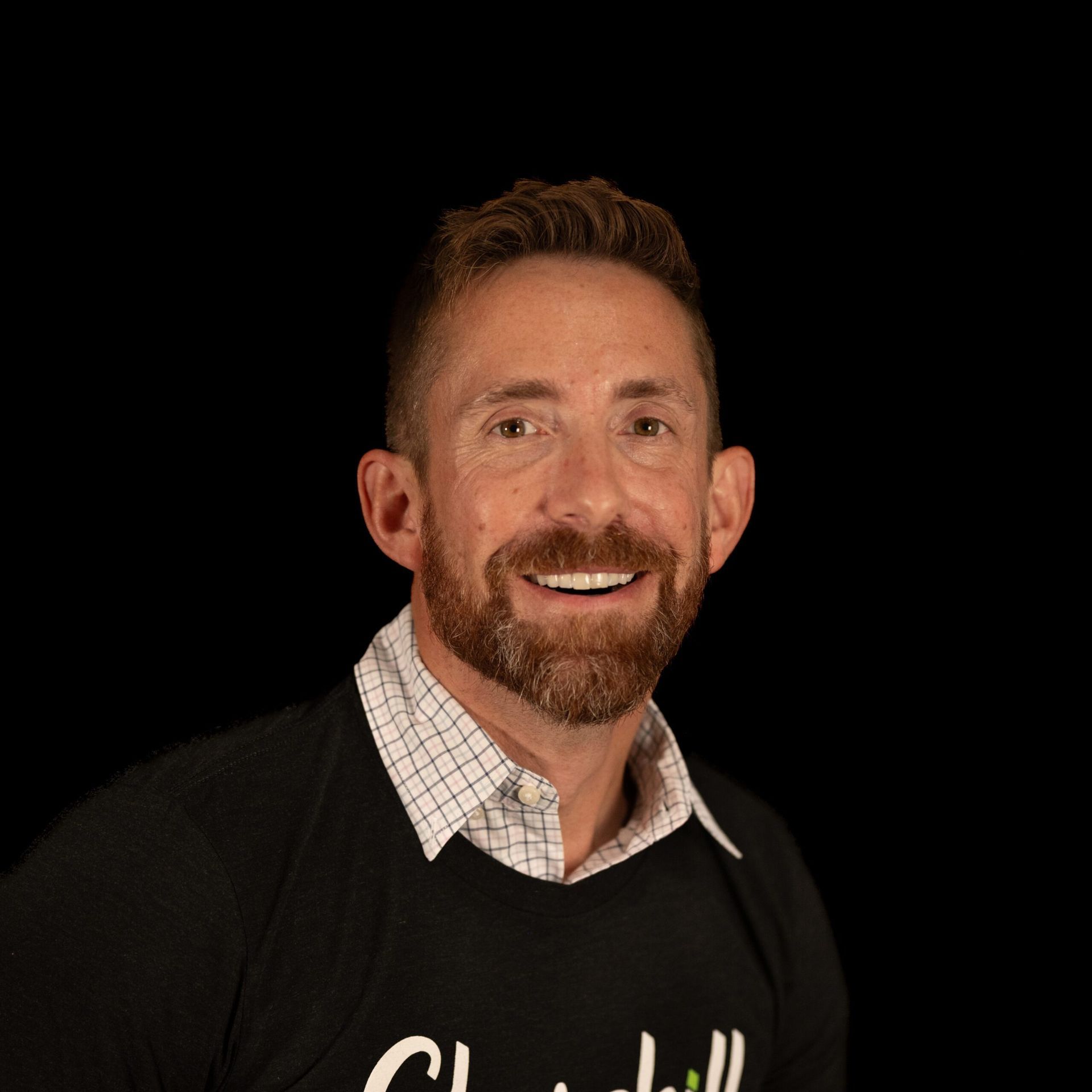 Man with a beard and a black sweater smiles. Black background.