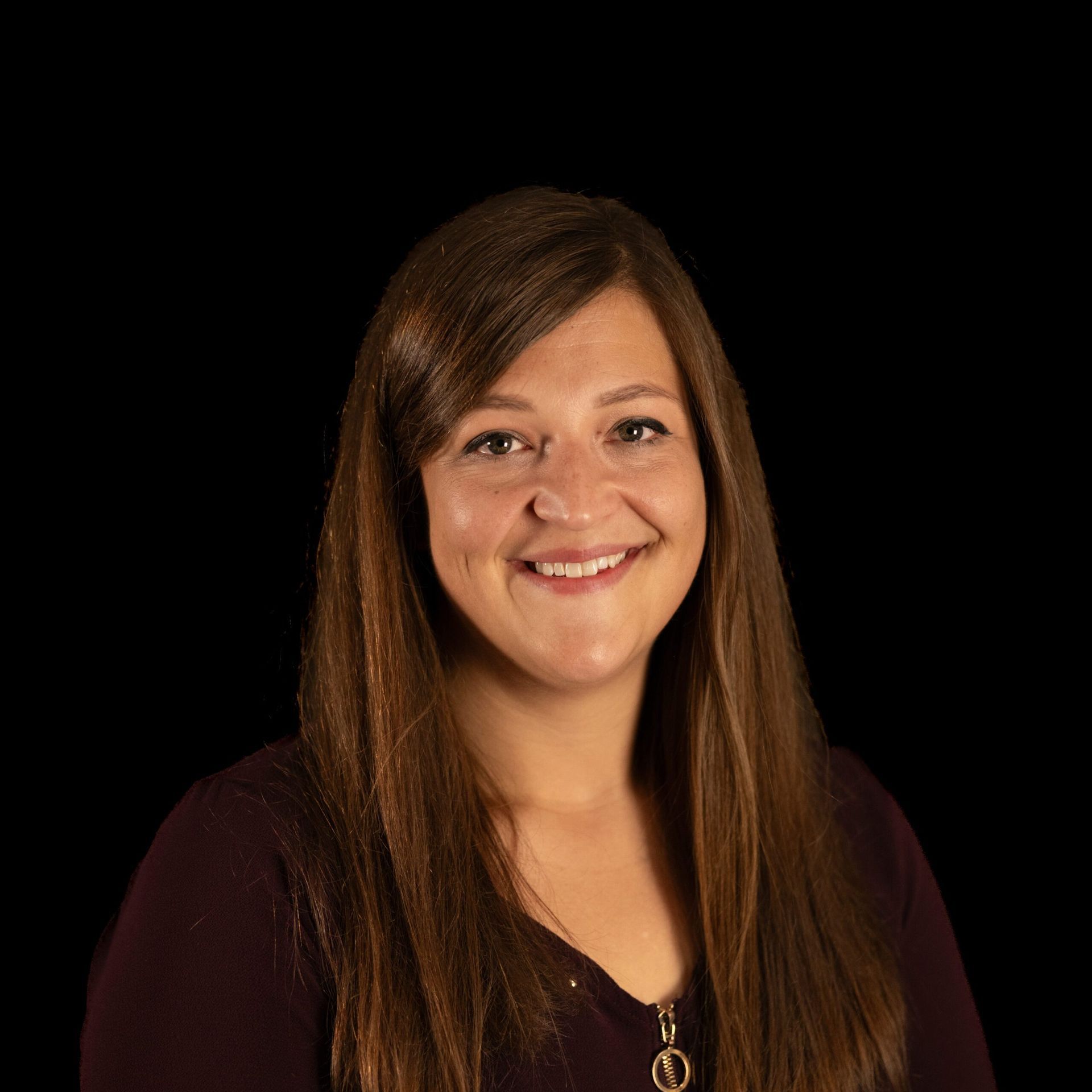 Woman with long brown hair smiles, wearing a burgundy top, set against a black background.