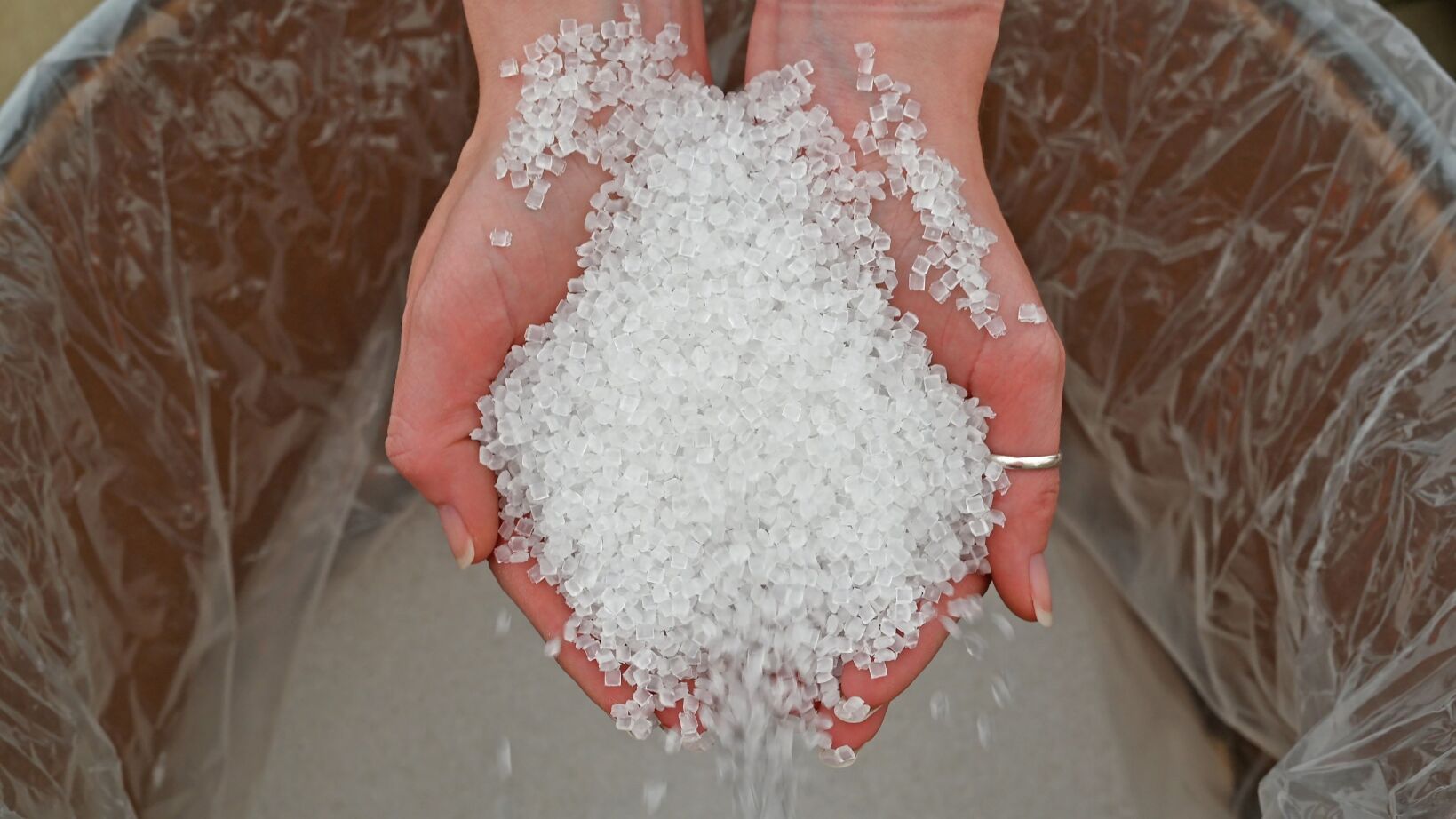 Hands holding a pile of translucent plastic pellets, spilling out from the palms.