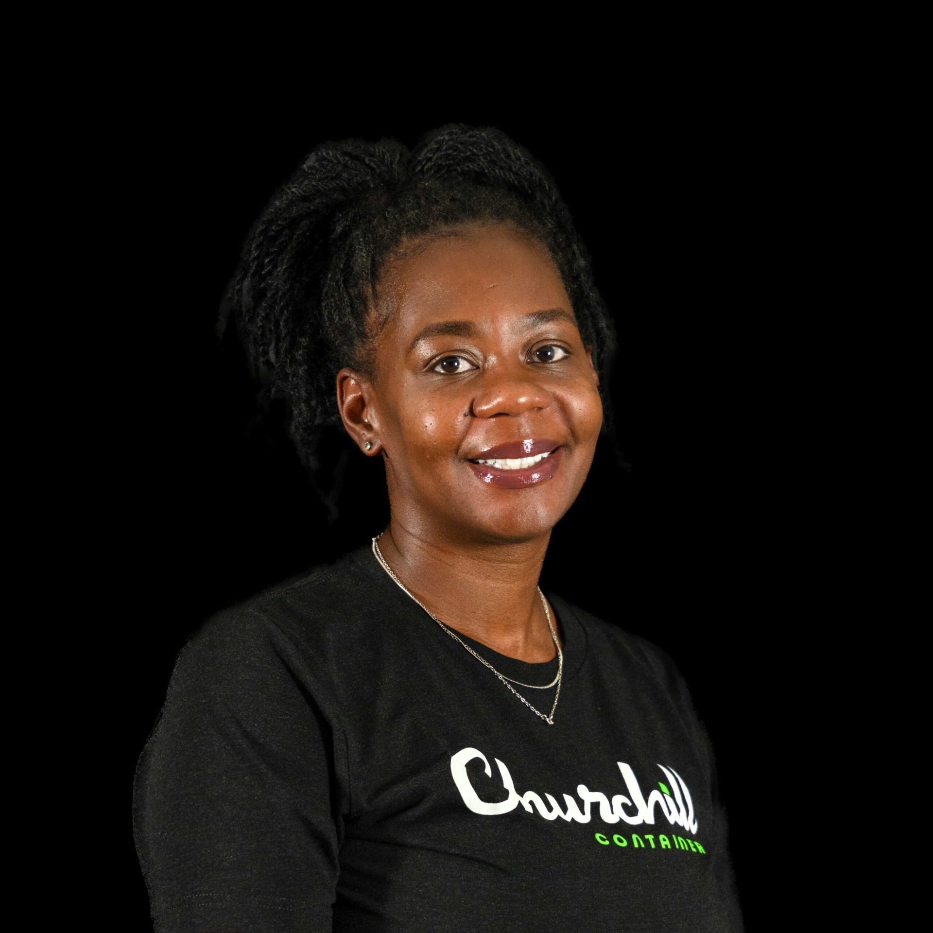 Woman in a black t-shirt smiles, a necklace around her neck, against a black background.