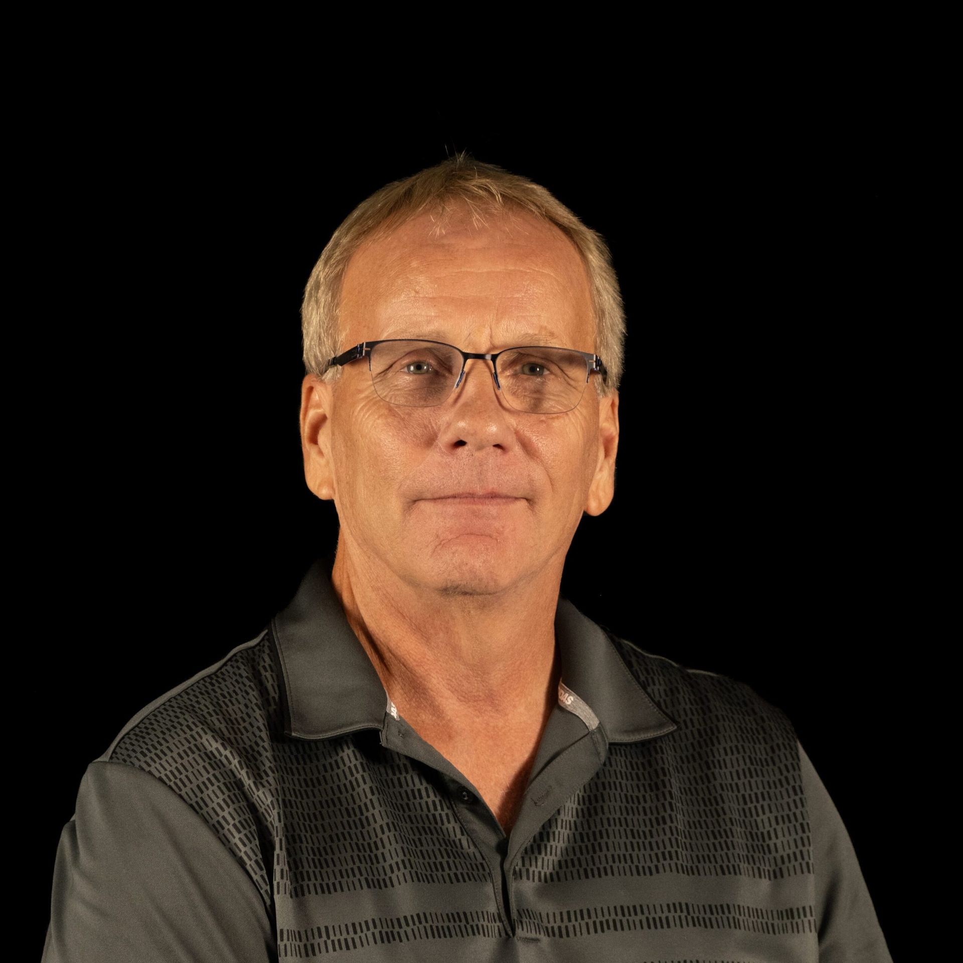 Man wearing glasses and a gray shirt, against a black background.