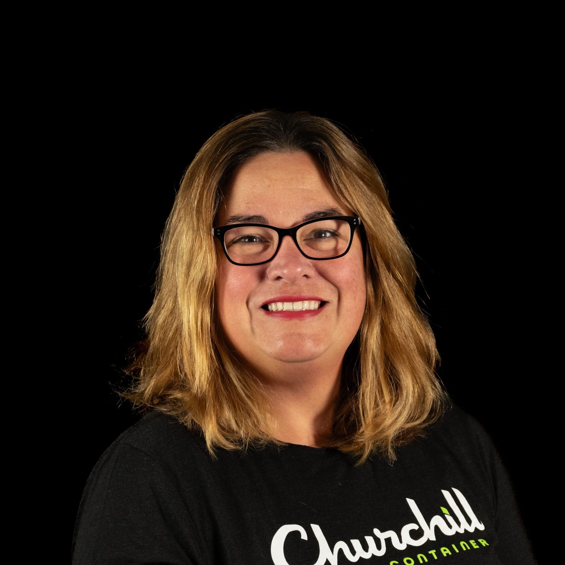 Woman with glasses and blonde hair smiling, wearing a black shirt with 