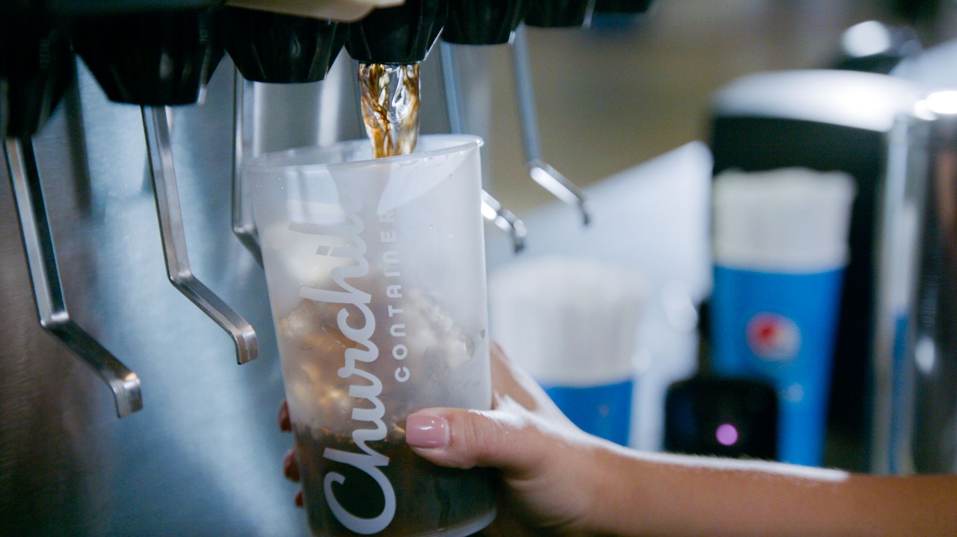 Person filling a Church’s Chicken branded cup with soda from a dispenser. The soda is dark and over ice.