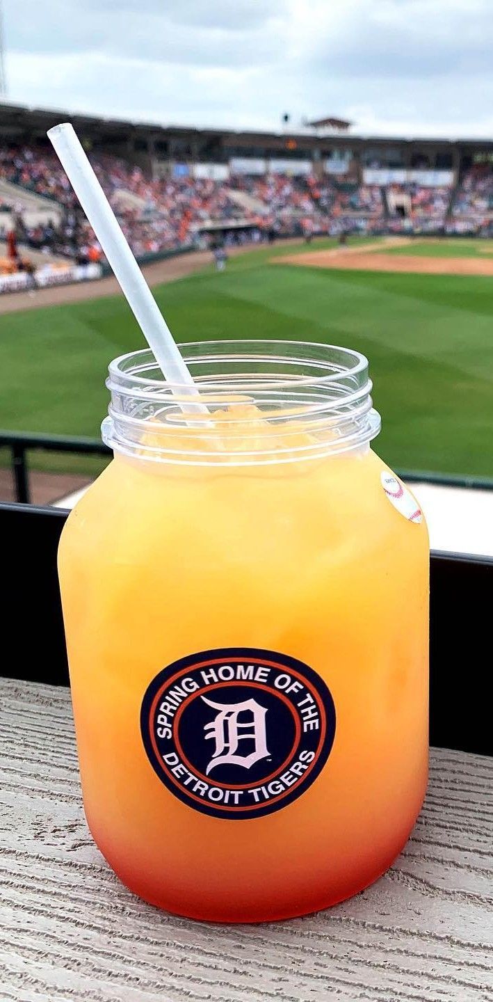 A layered orange drink with a straw in a mason jar at a baseball stadium.