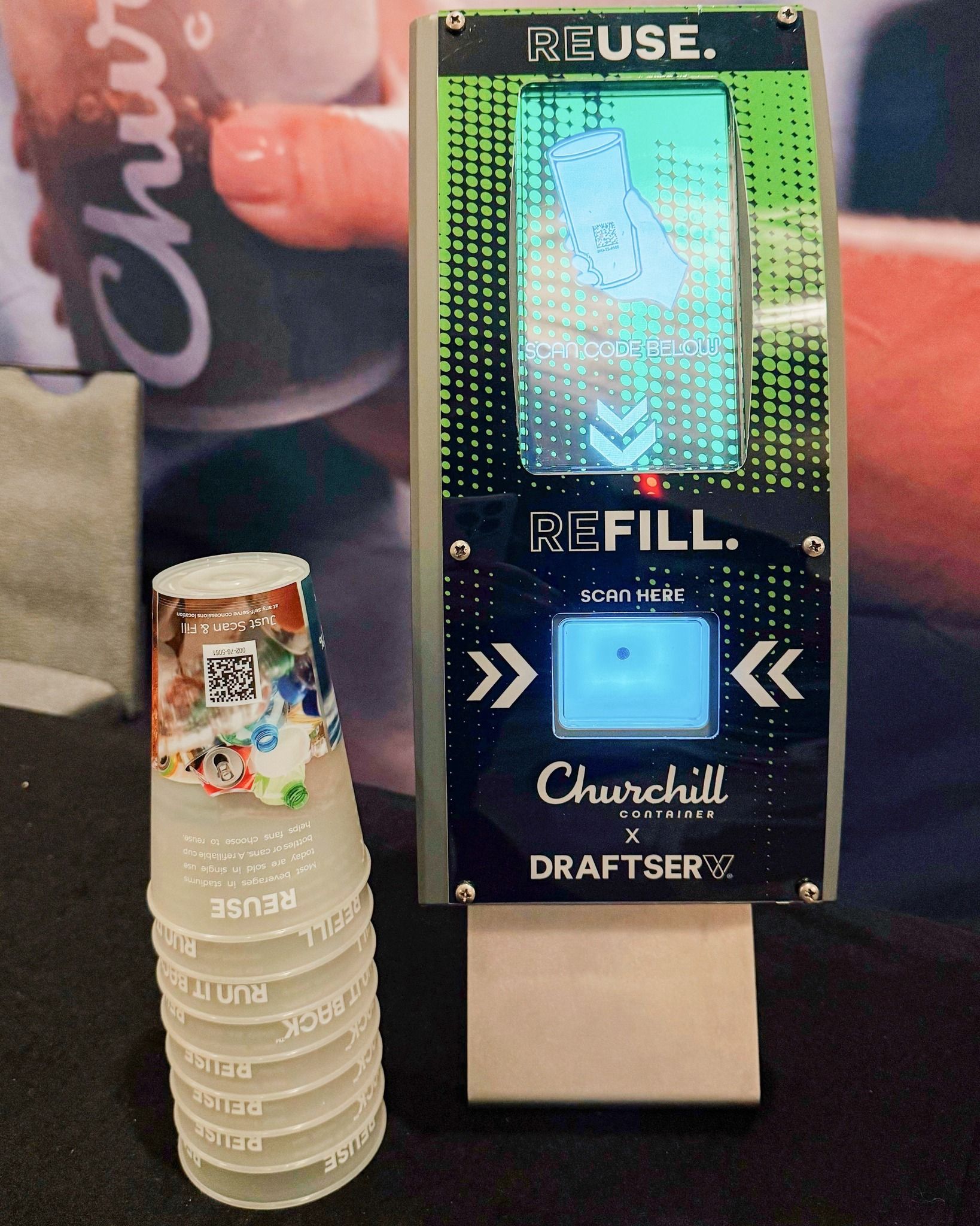 Stack of clear cups next to a reusable drink dispenser with a screen and “REFILL” label.