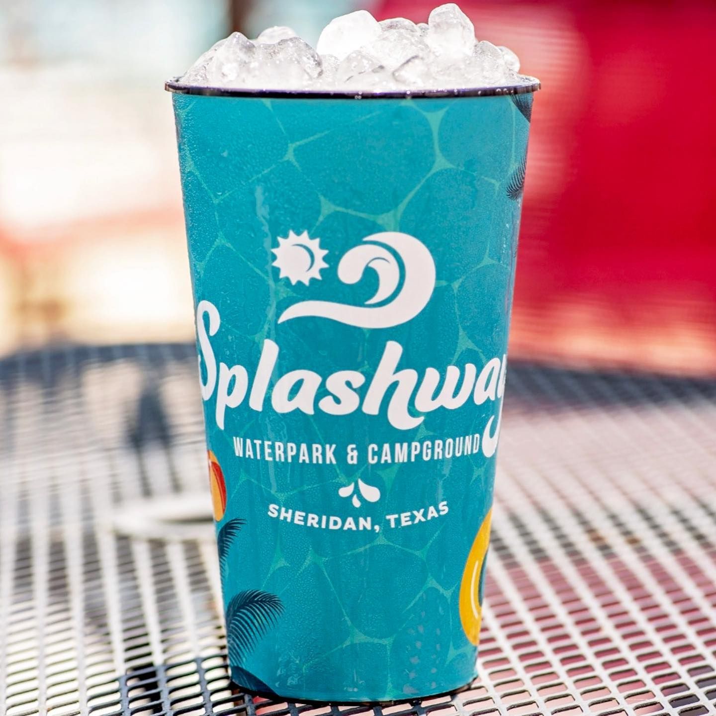 A turquoise Splashway Waterpark cup filled with ice on a patio table.