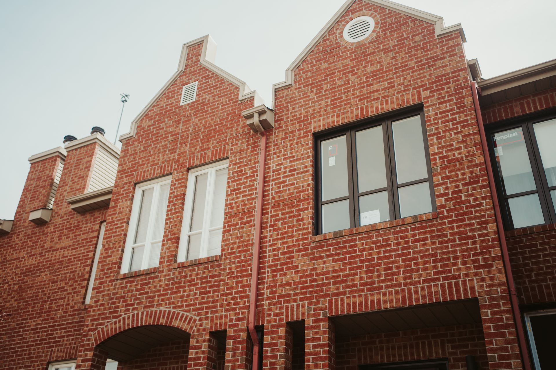 Maisons de ville en briques rouges avec entrée en arc, fenêtres et pignons décoratifs contre un ciel clair.