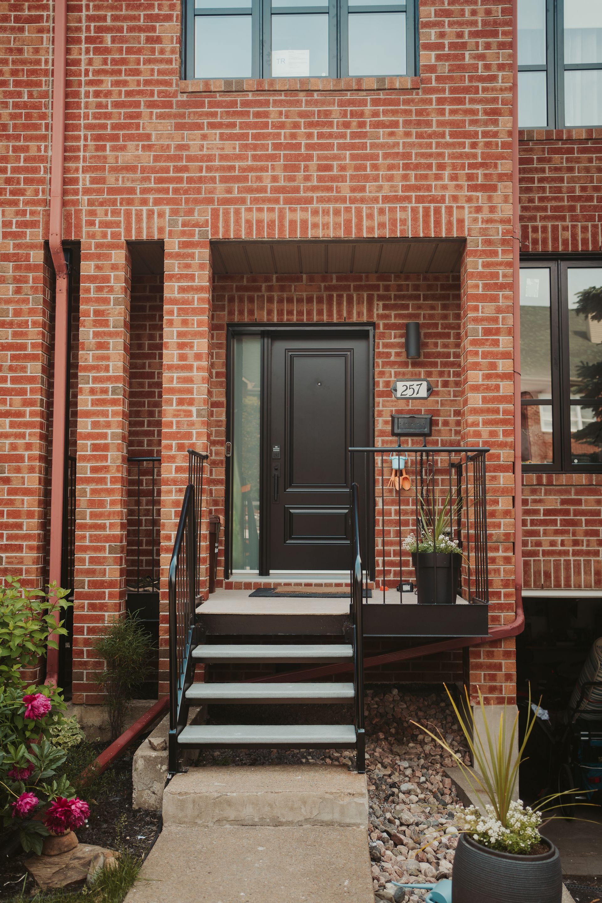 Red brick townhouse exterior with black door, steps, and railings.