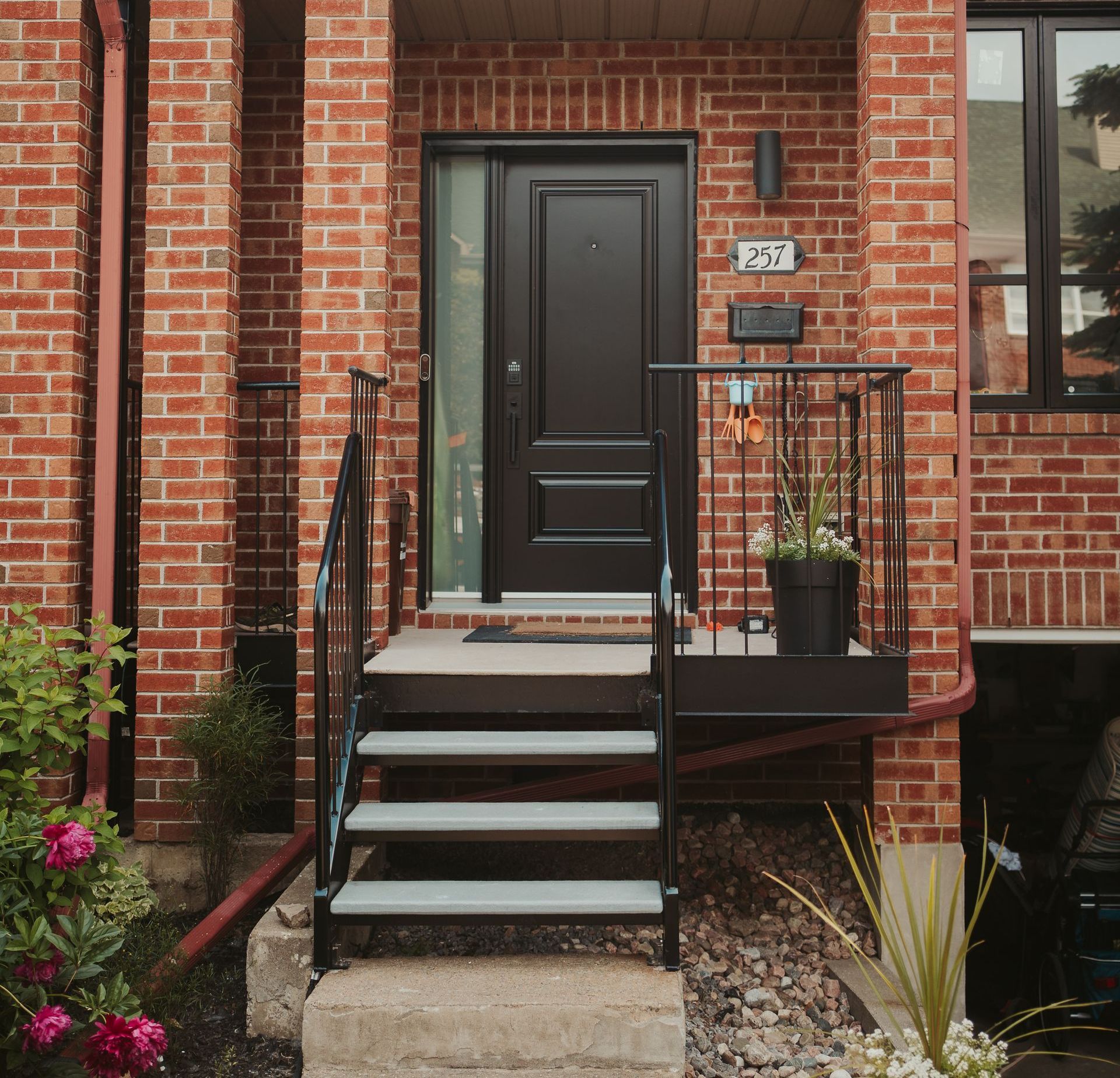 Entrée de maison de ville en brique avec marches, porte noire et balustrade.