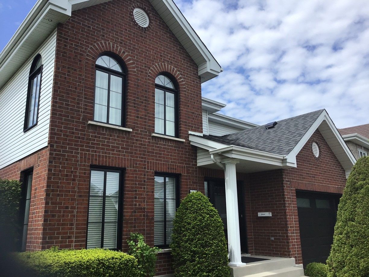 Maison à deux étages en brique et revêtement blanc avec fenêtres cintrées à cadre noir et porte de garage noire.