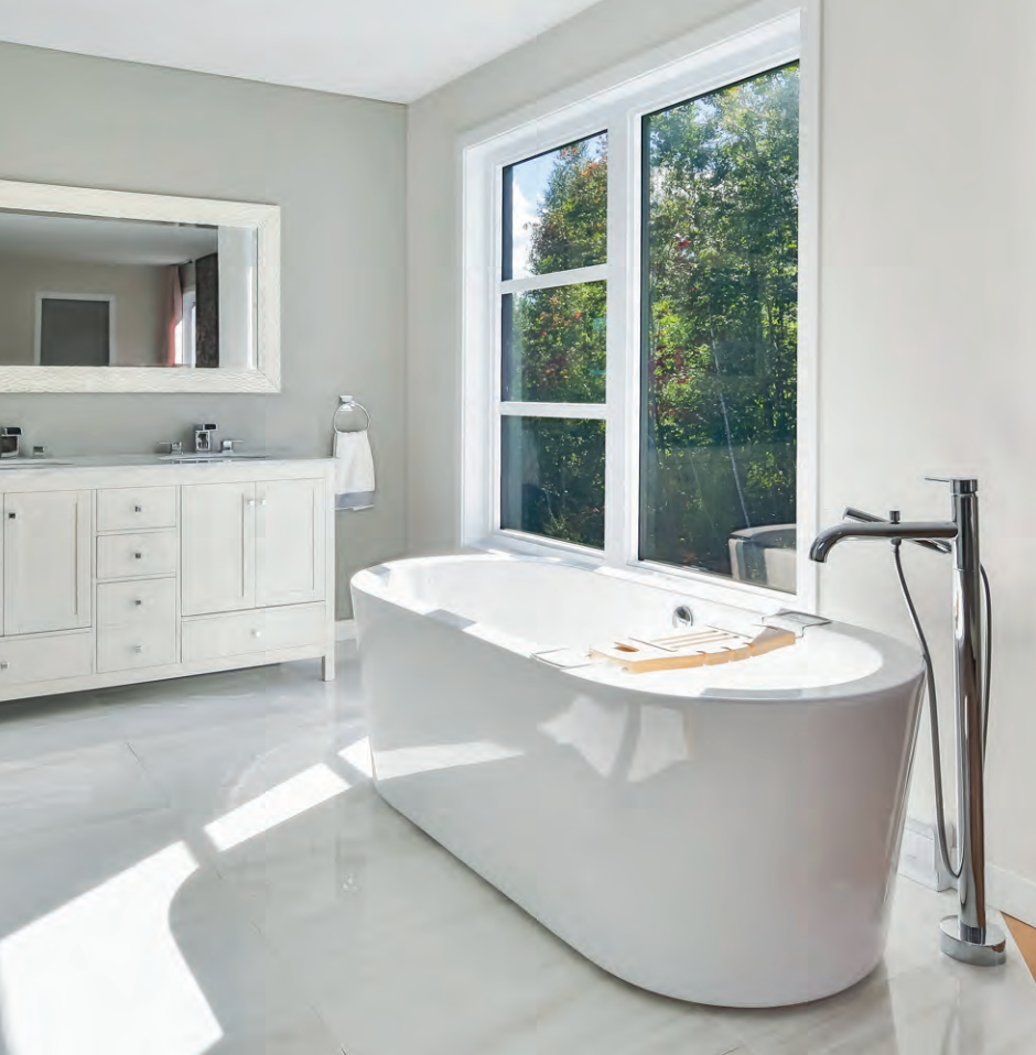 Salle de bain blanche et lumineuse avec baignoire autoportante, grande fenêtre et vanité blanche.