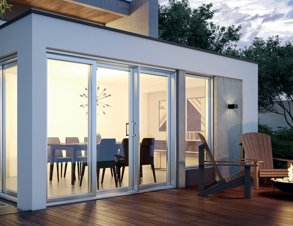 Patio with large glass doors, showing dining table inside. Wooden deck, chairs, and trees visible.
