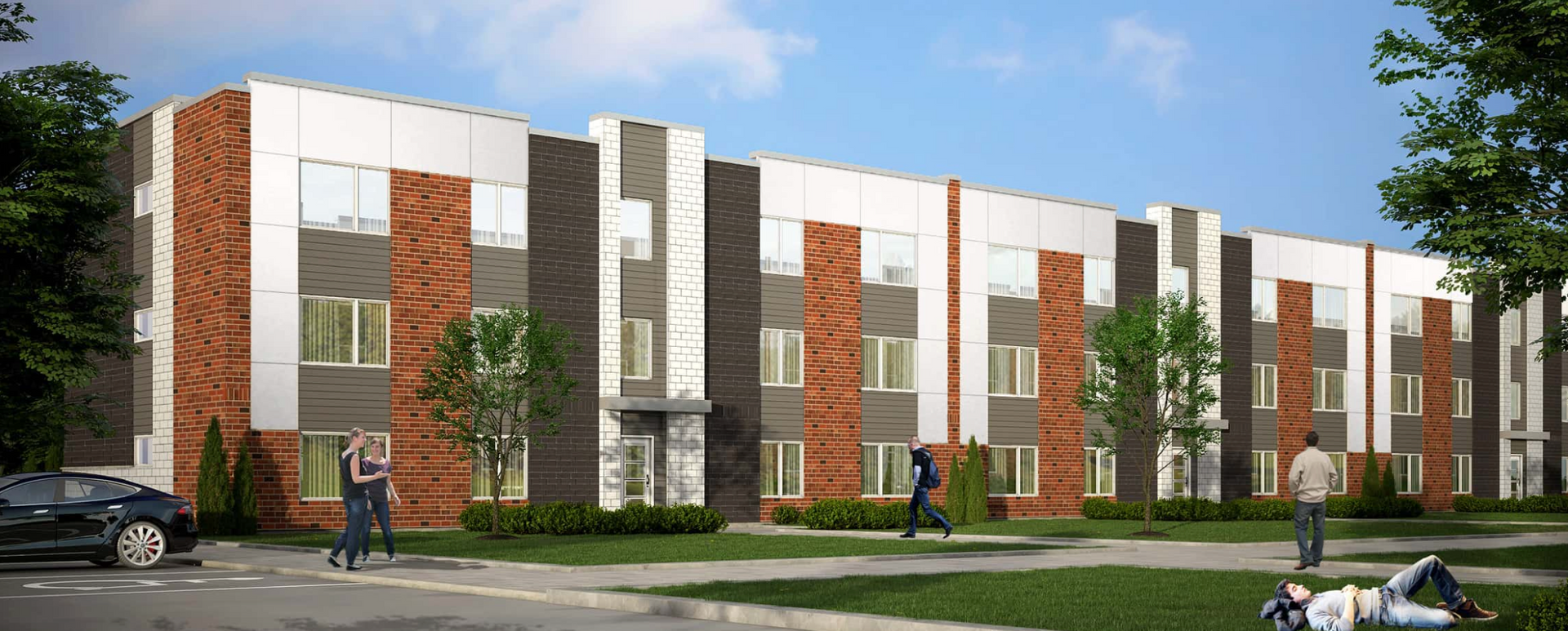 A multi-story building with white, gray, and brick-colored panels. People are walking on the lawn and sidewalk.