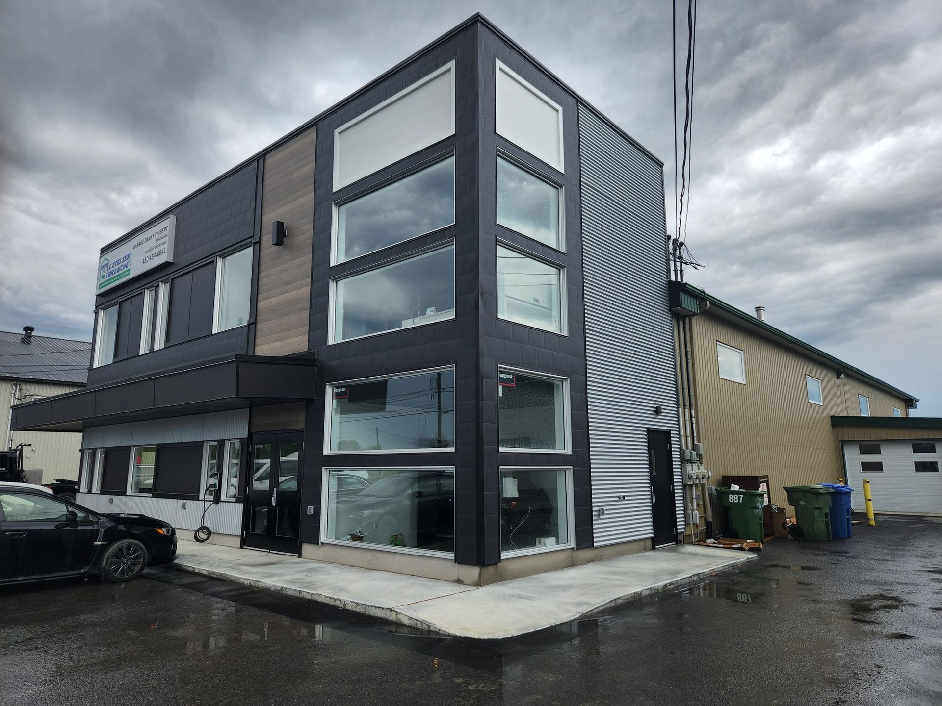 Bâtiment moderne noir et marron avec de grandes fenêtres et un fond de ciel nuageux.