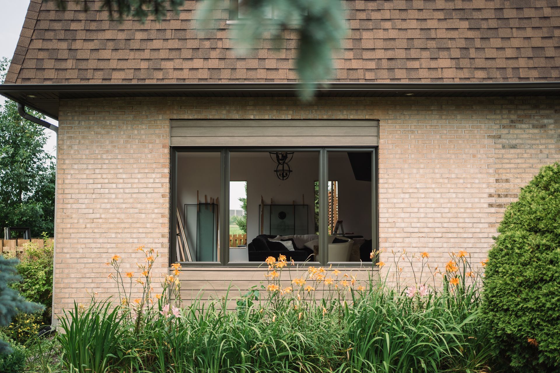 Brick building with a large window, brown roof, and garden in front.