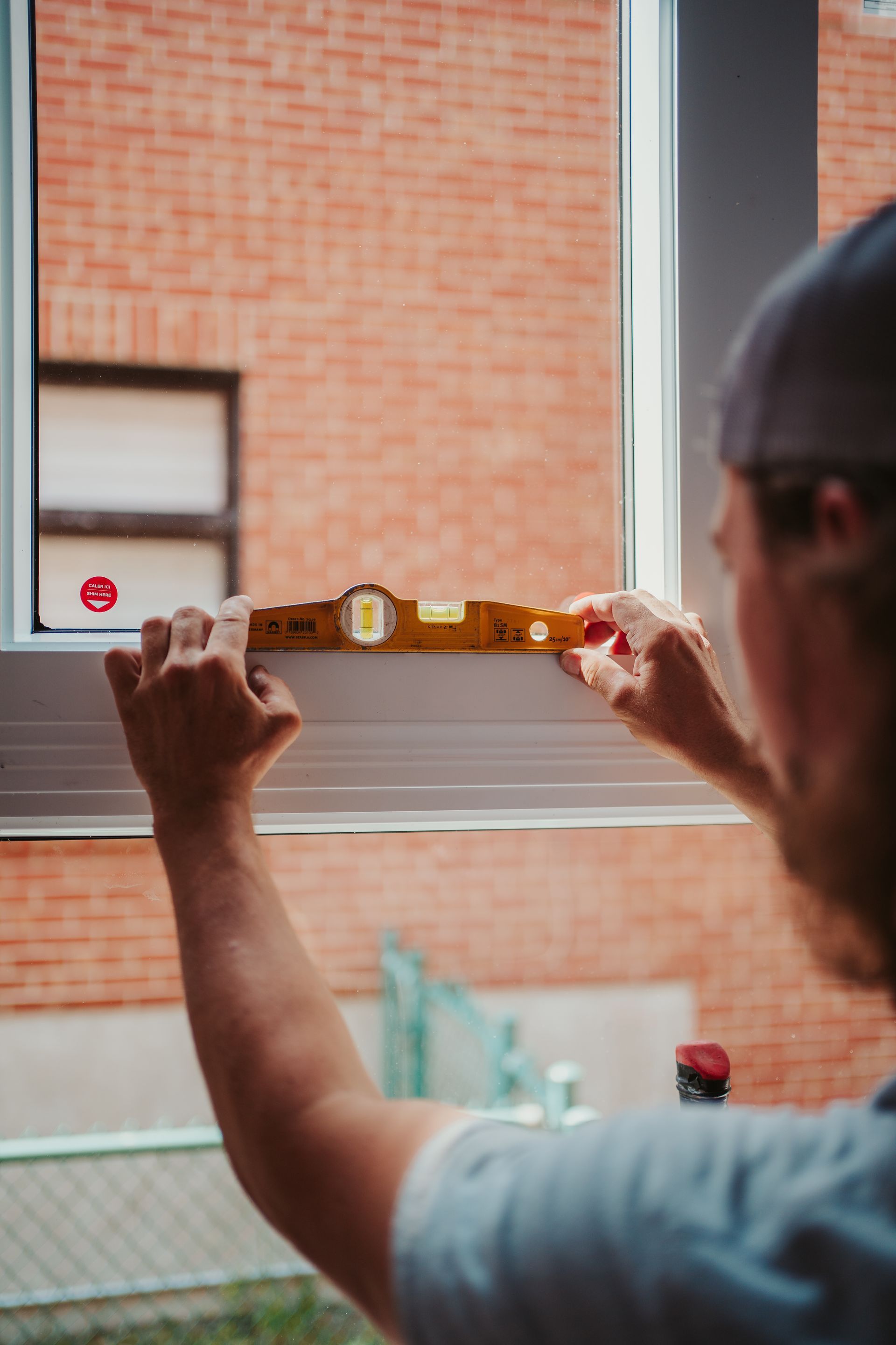 Personne utilisant un niveau sur un cadre de fenêtre, vérifiant l'alignement contre un mur de briques.