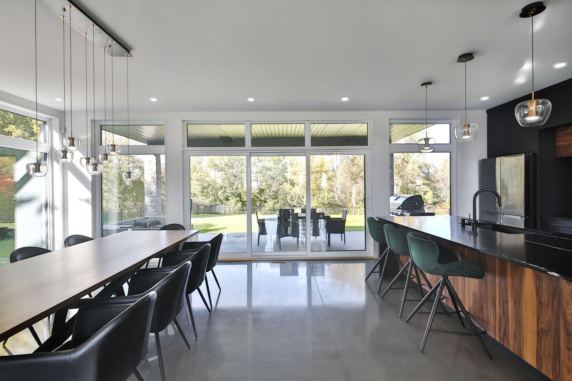 Modern open-concept kitchen with long island, dining table, and large windows overlooking a bright patio