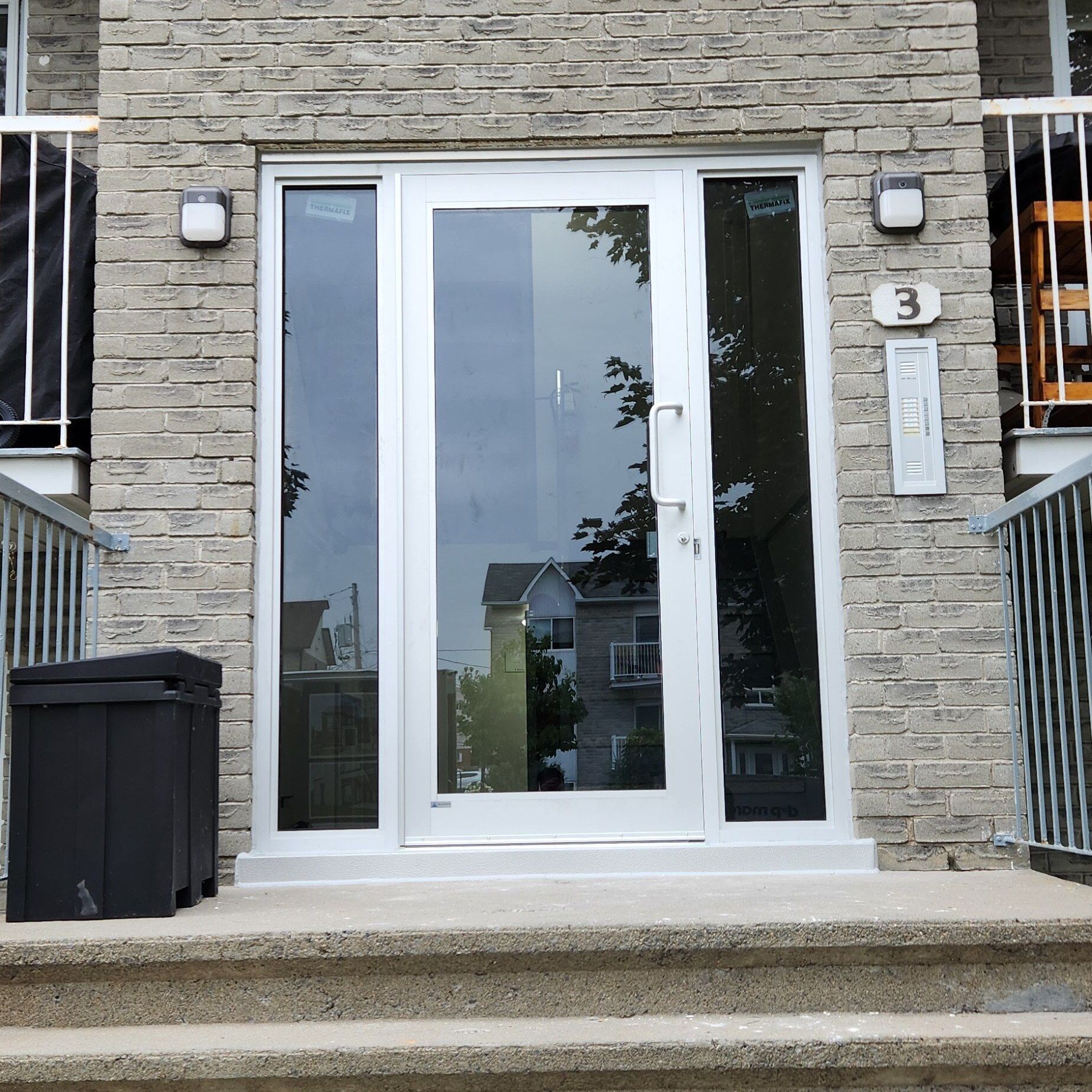 Un bâtiment en briques avec une porte blanche et une poubelle noire