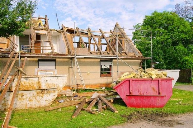 A house is being demolished and a red dumpster is in front of it.