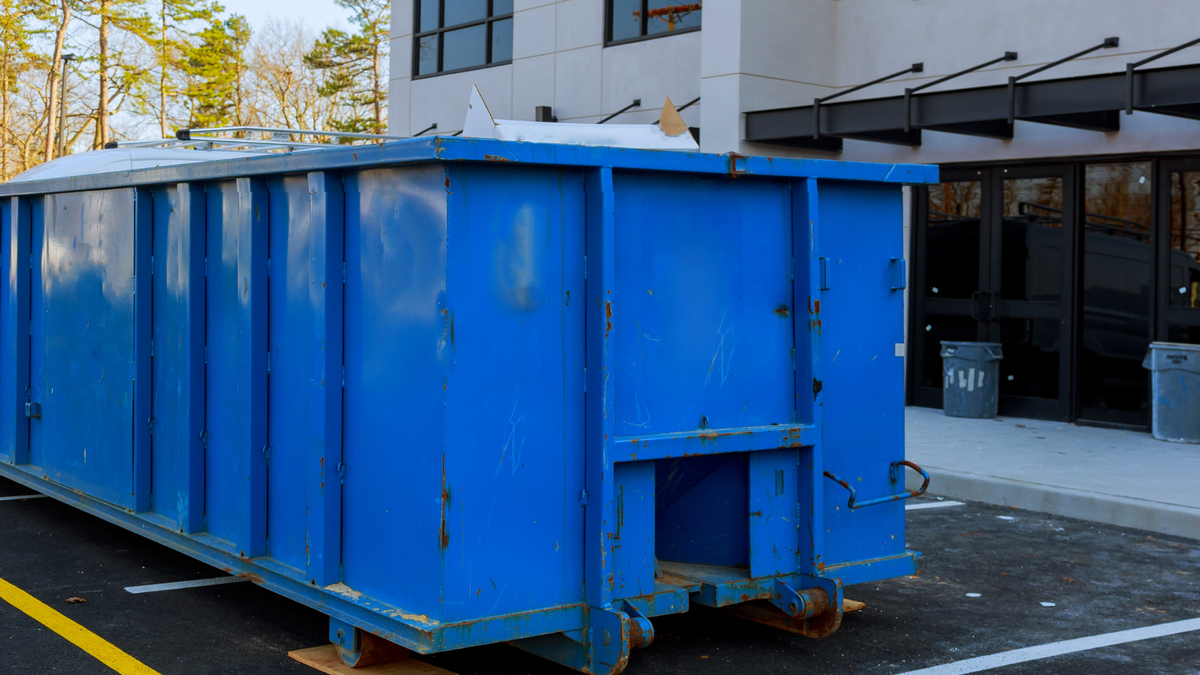 A large blue dumpster is parked in front of a building.