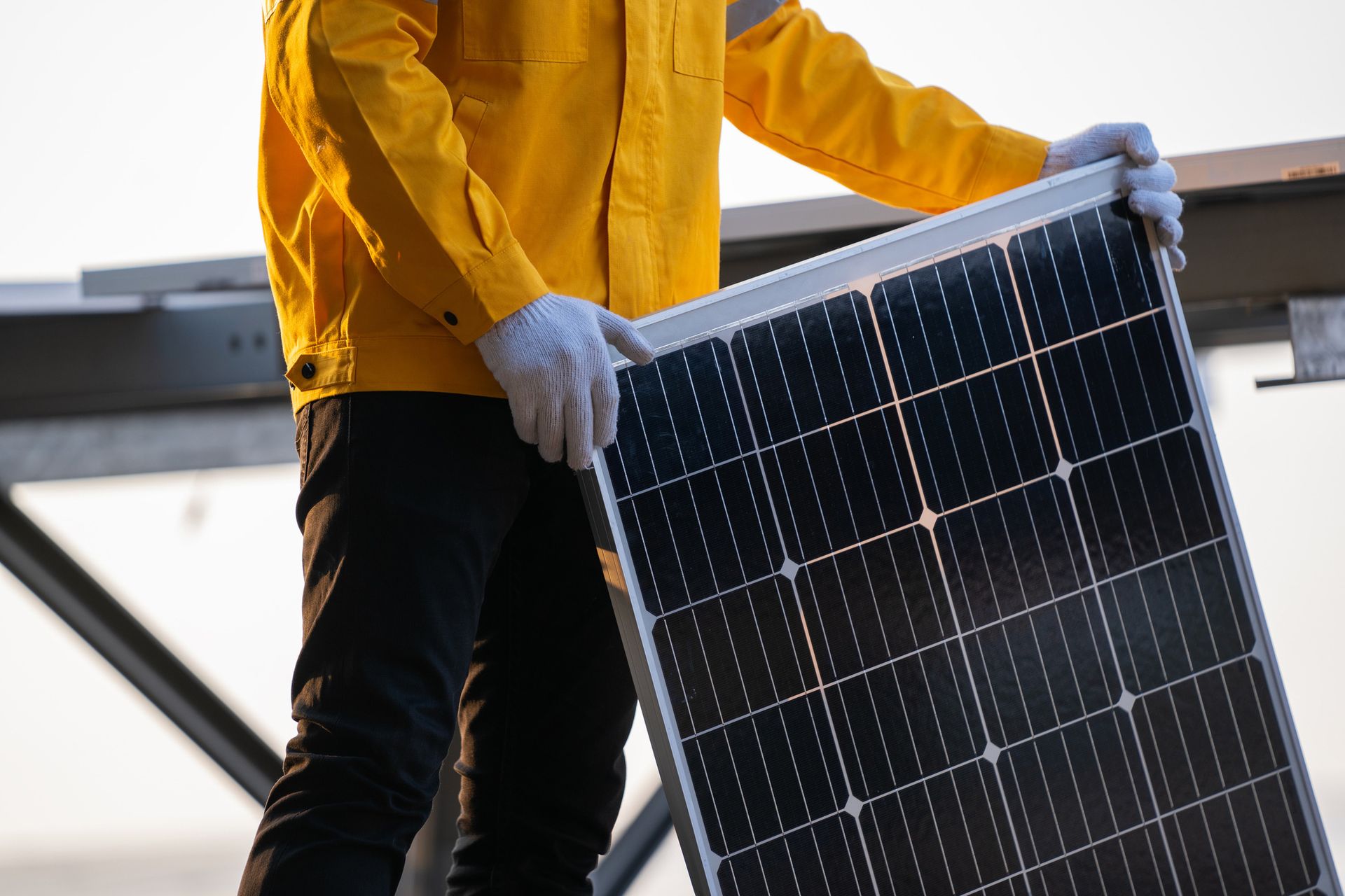 Person in yellow jacket holding a solar panel on a rooftop.