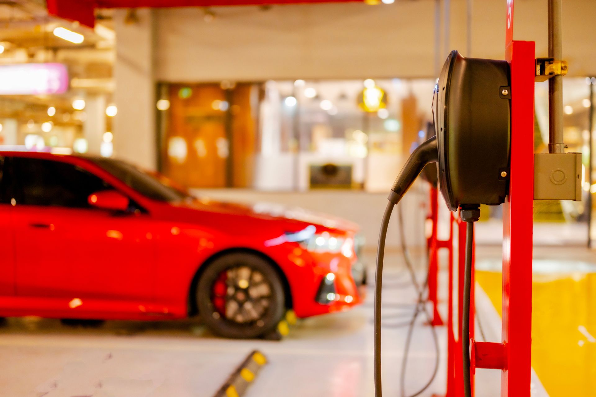 Red electric car charging at a charging station in a parking garage.