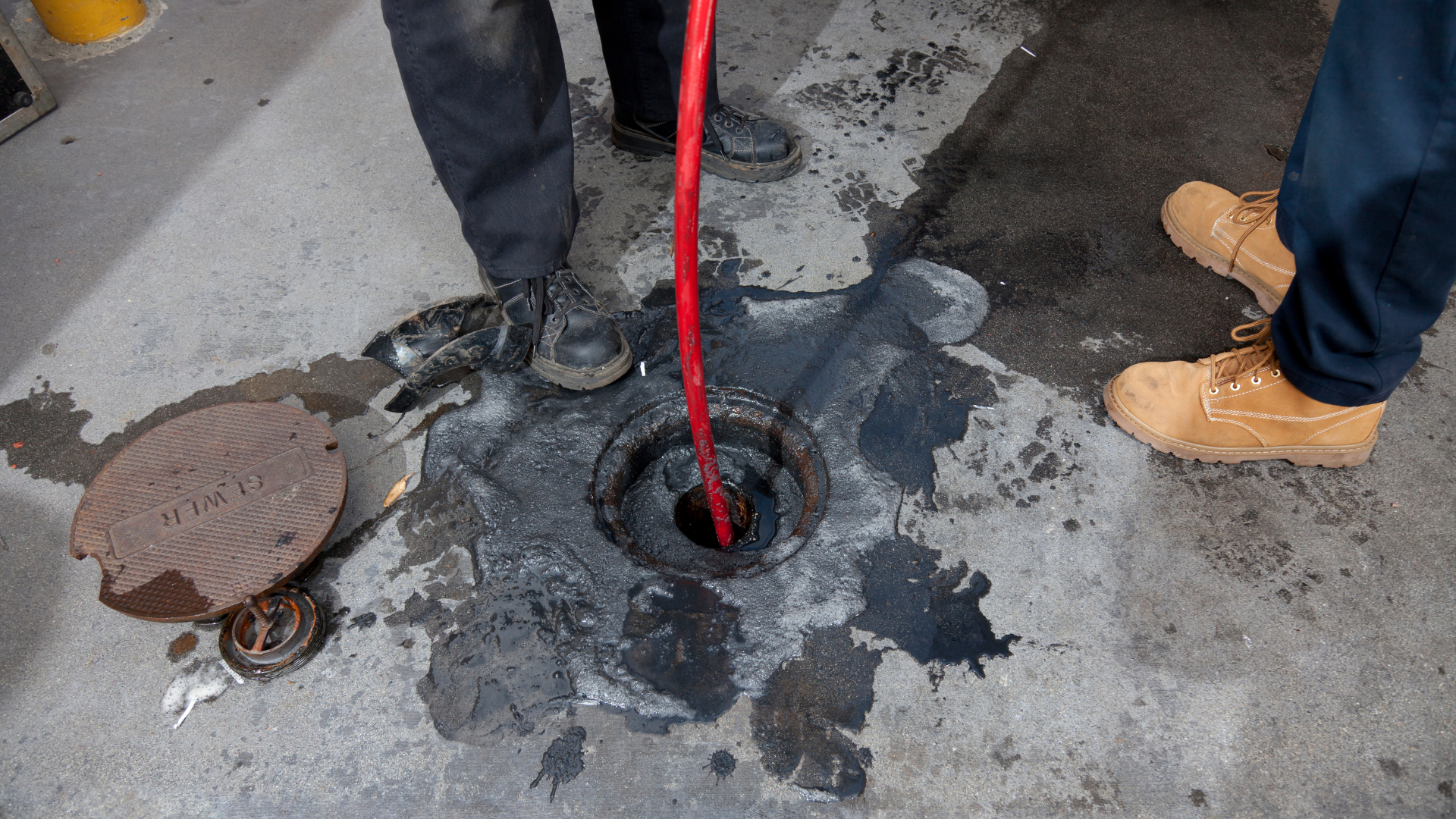 A manhole cover with a red hose sticking out of it.