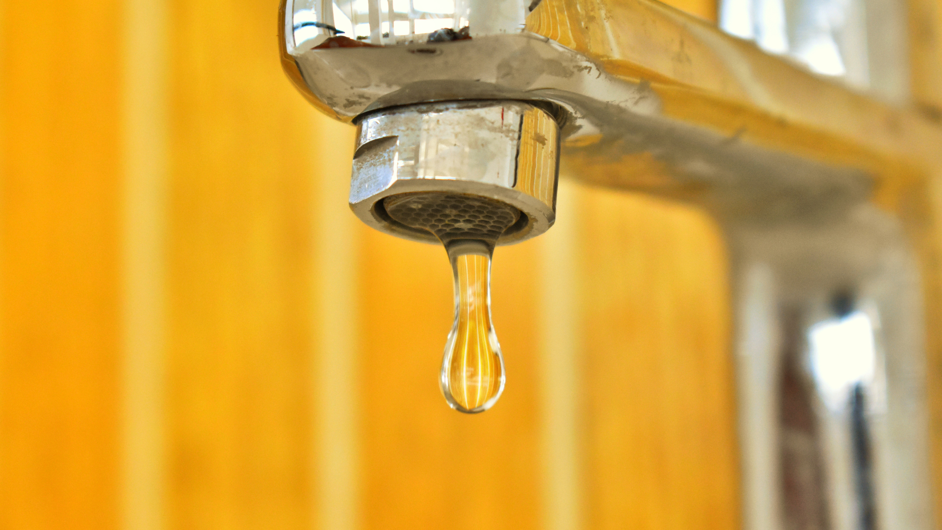 A close up of a faucet with a drop of water coming out of it.