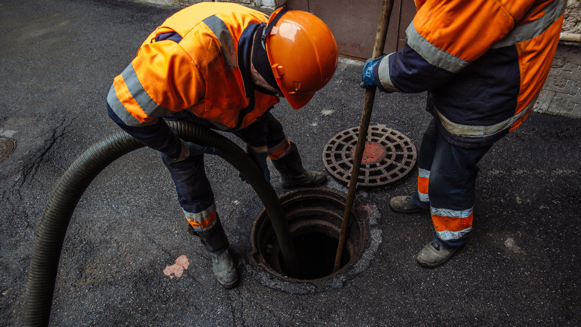 Two men are cleaning a manhole cover with a hose.