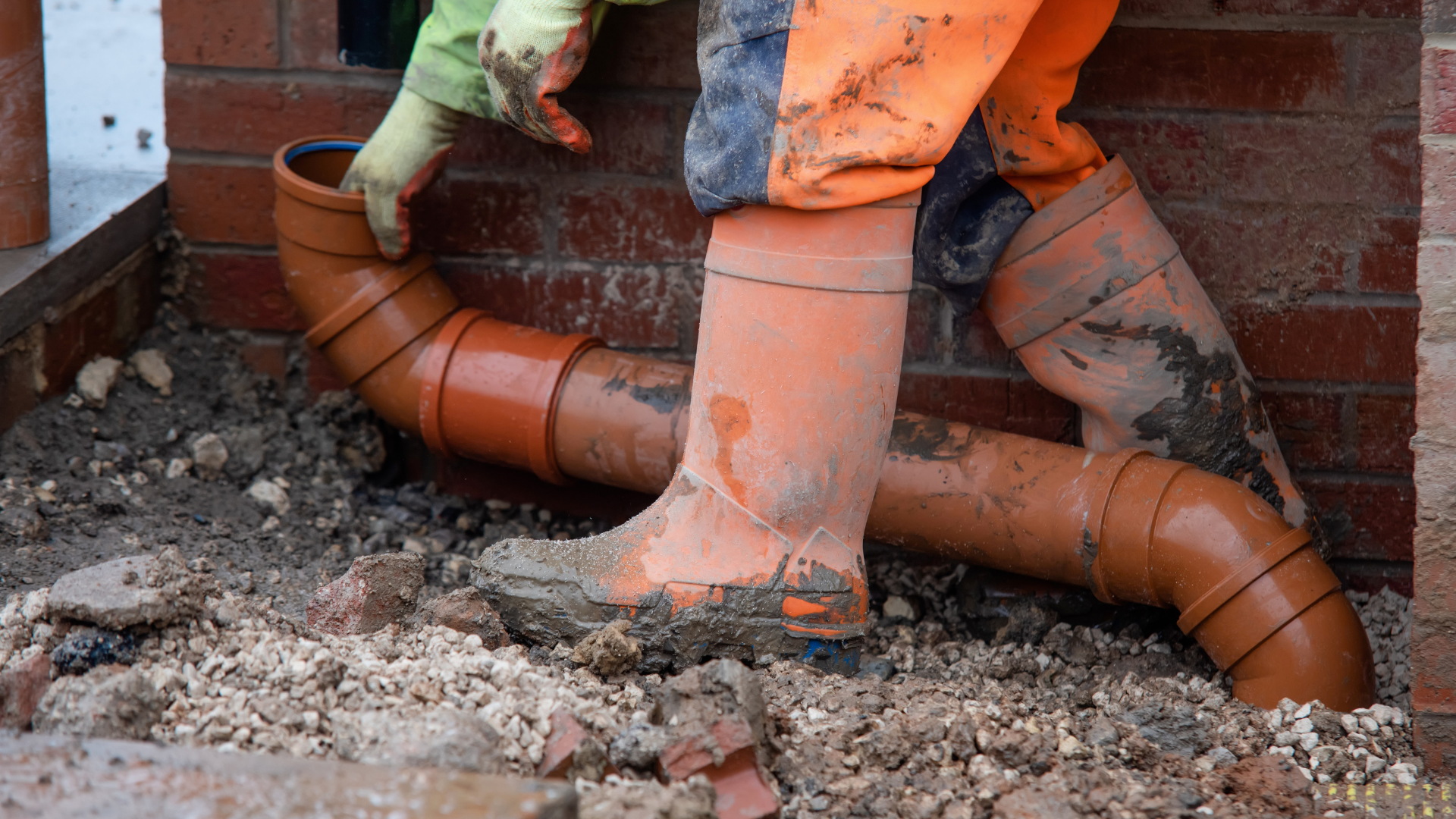 A person wearing orange boots is working on a drain pipe.