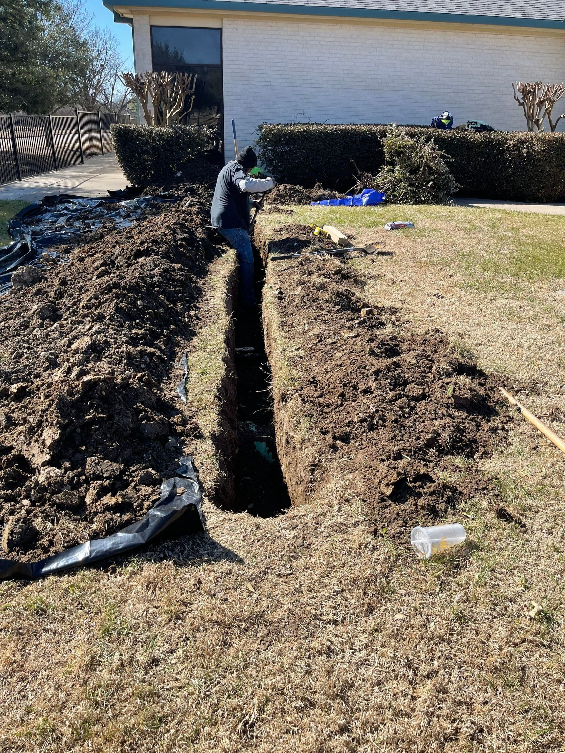 A man is digging a hole in the ground in front of a house.