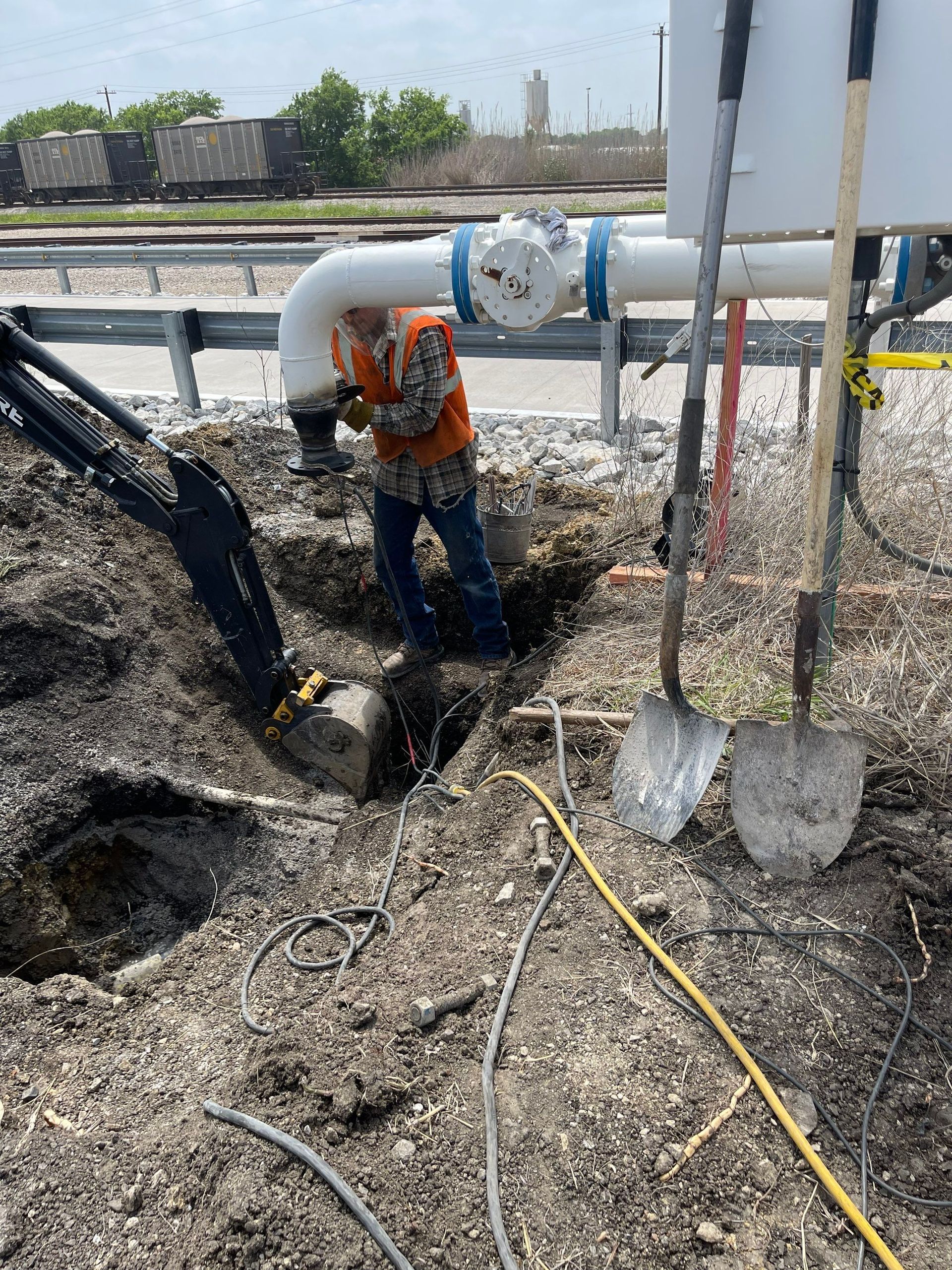 A man is digging a hole in the ground next to a pipe.