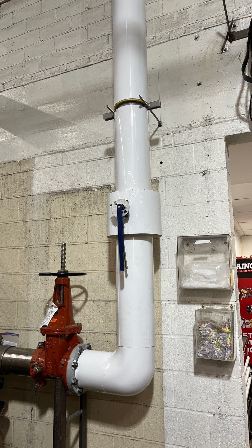 A white pipe is attached to a red valve in a room.