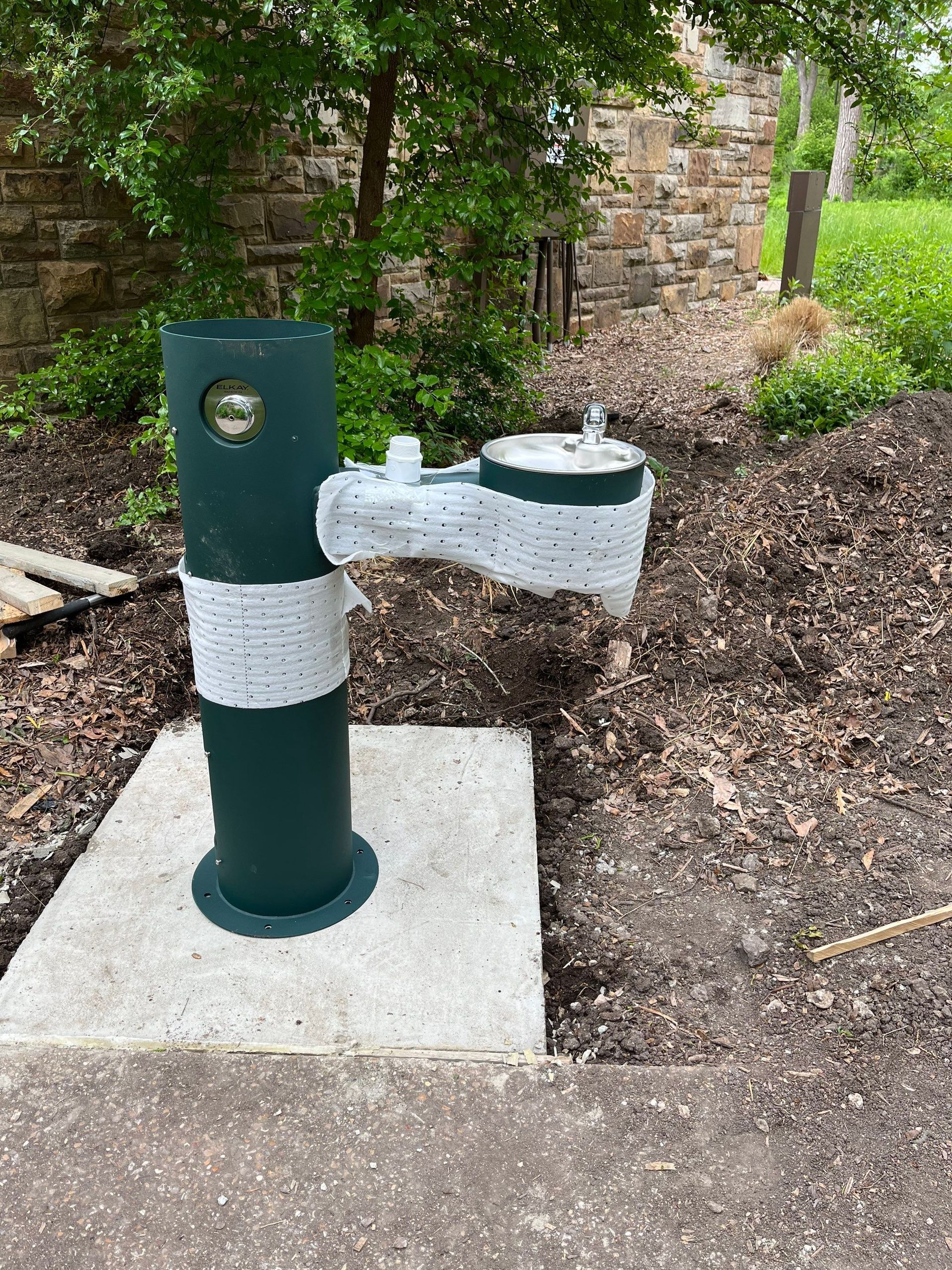 A water fountain is sitting on a concrete base in a park.