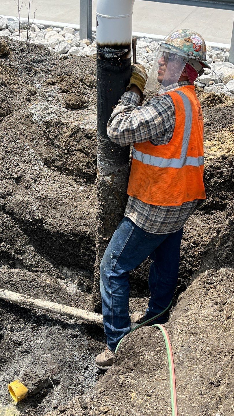 A construction worker is standing in the dirt holding a pipe.