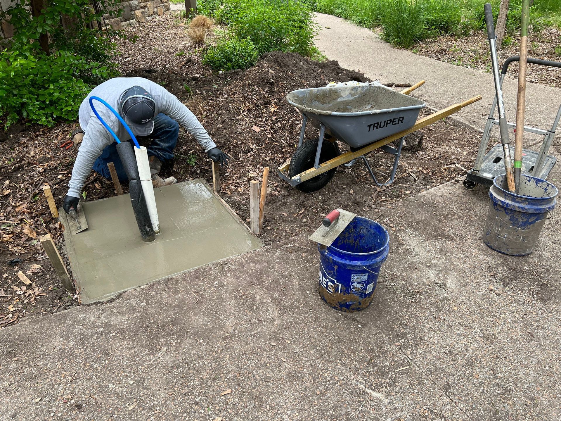 A man is pouring concrete on a sidewalk next to a wheelbarrow.